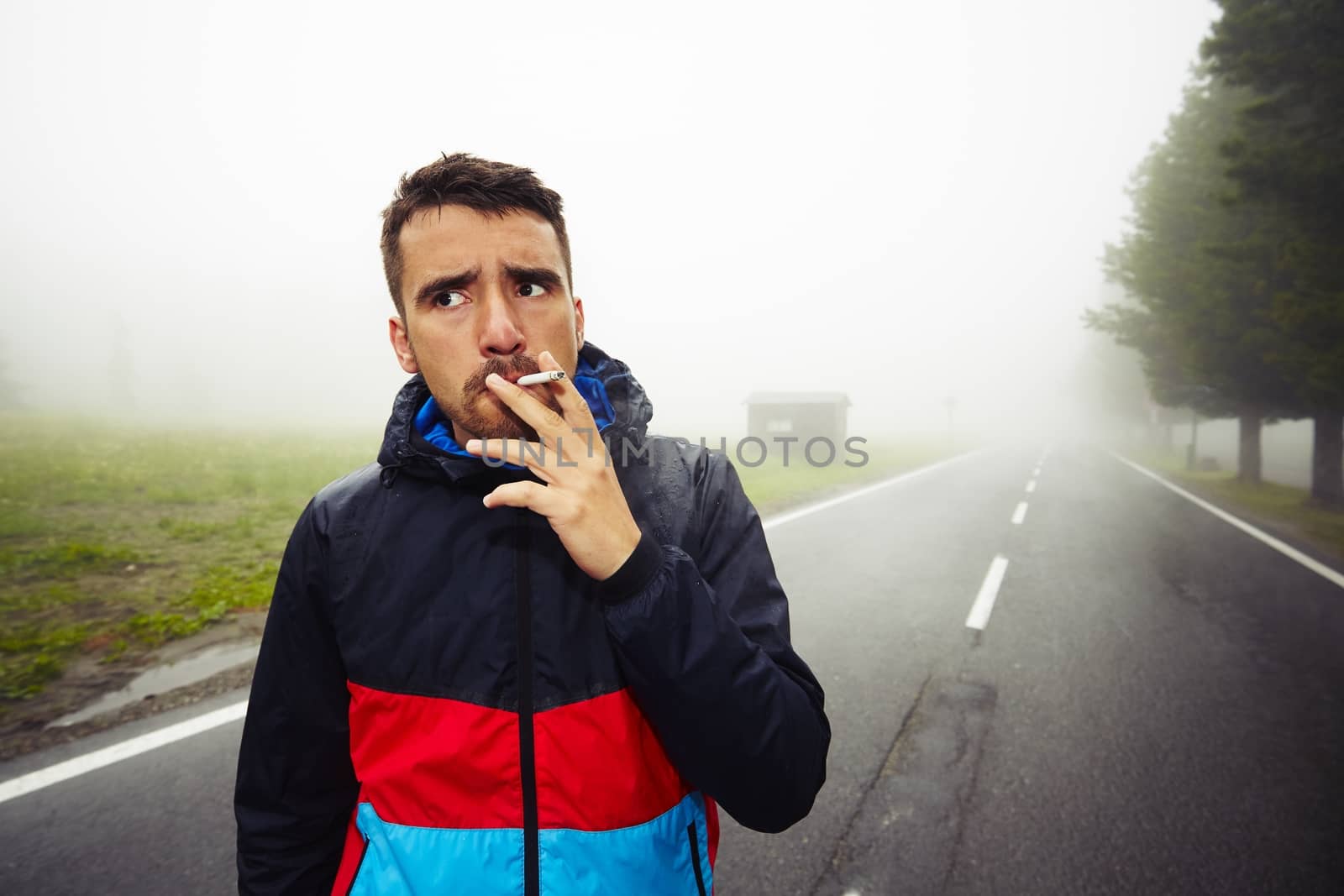 Young man is smoking on the road in mysterious fog