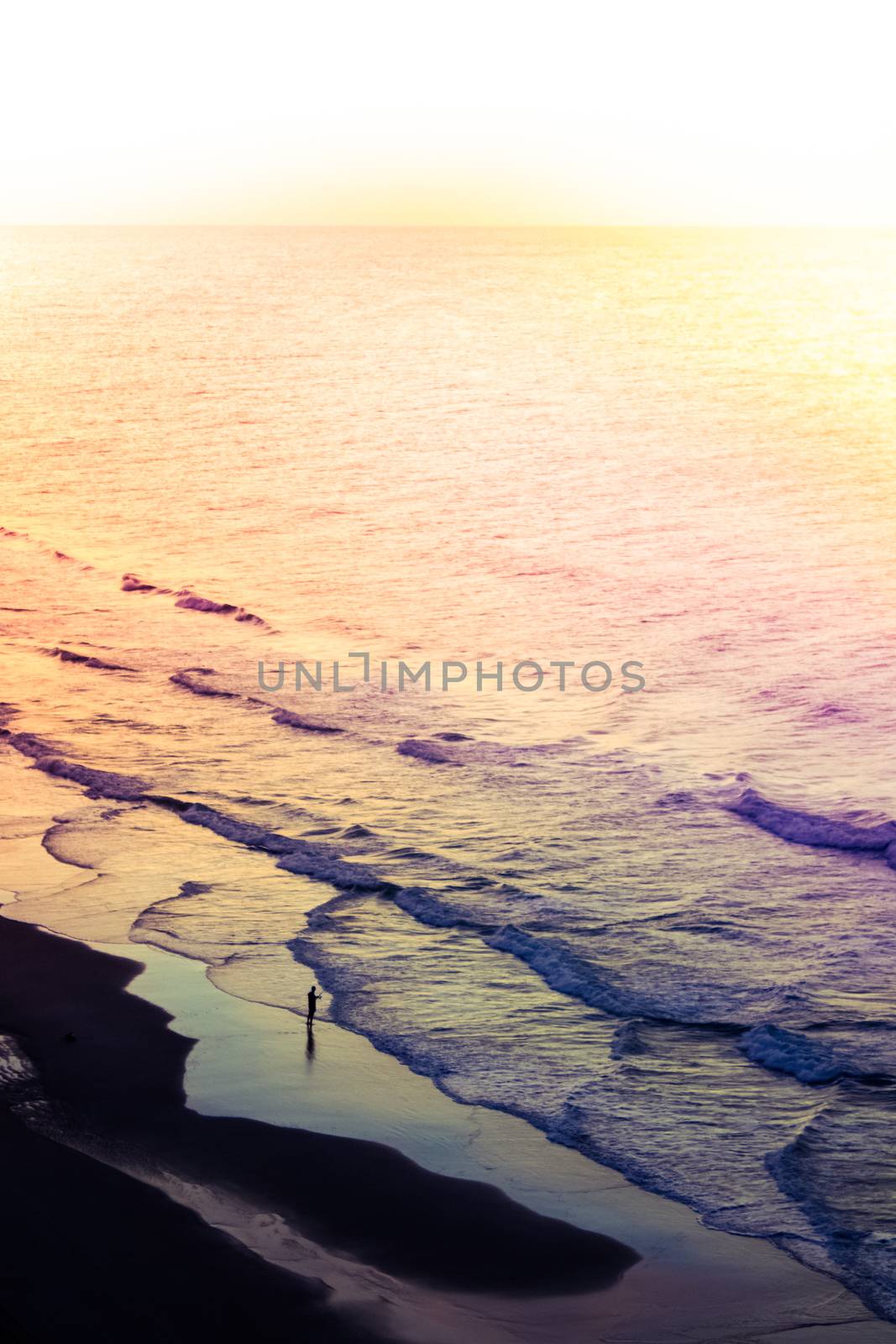 A colorful sunrise on the shoreline of a beach with a surf fisherman.