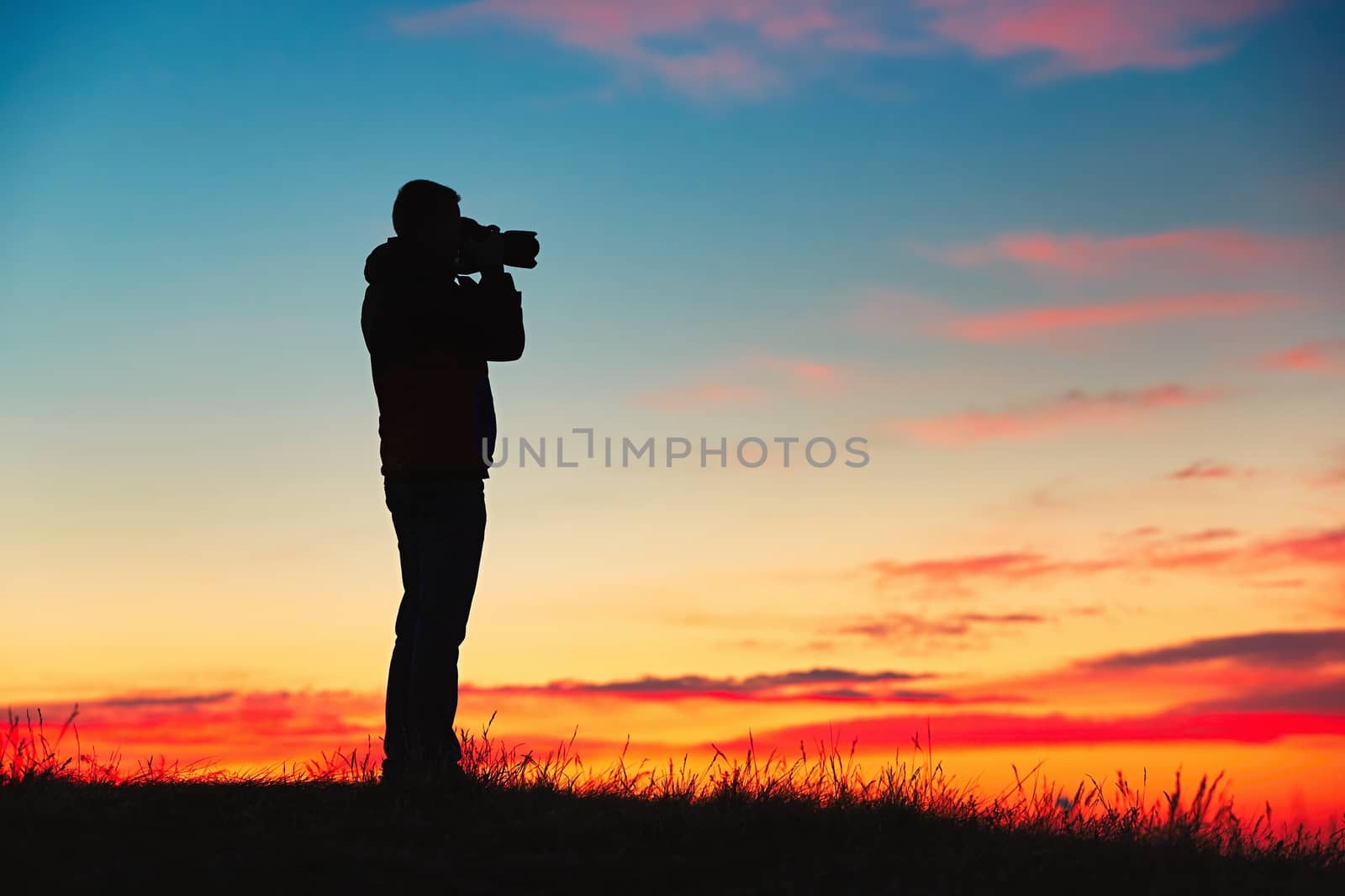 Silhouette of young photographer is enjoying sun. Photographer with mirror camera is ready to take sunrise pictures. 
