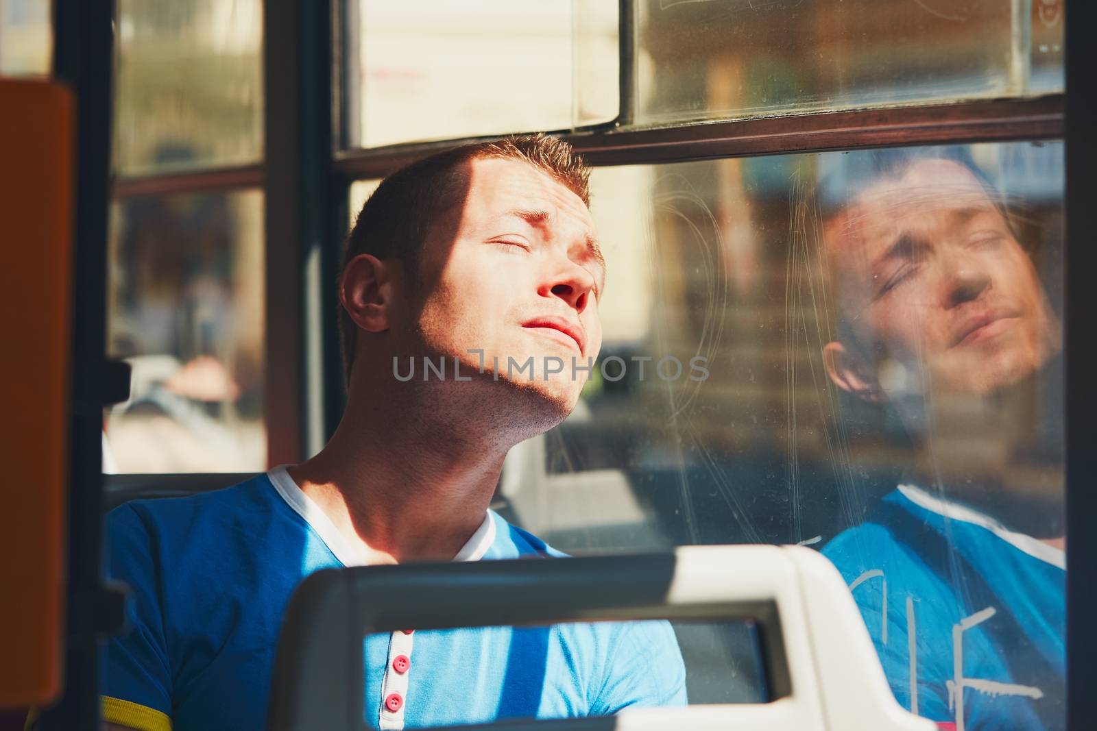 Everyday life and commuting to work by public transportation. Handsome young man is traveling by tram (bus). Tired man in hot day. Prague, Czech Republic