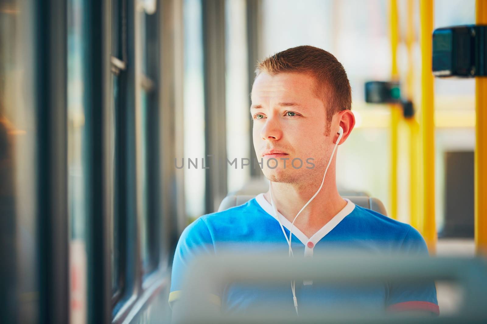 Everyday life and commuting to work by public transportation. Handsome young man is traveling by tram (streetcar). Man is wearing headphones and listening to music. Prague, Czech Republic
