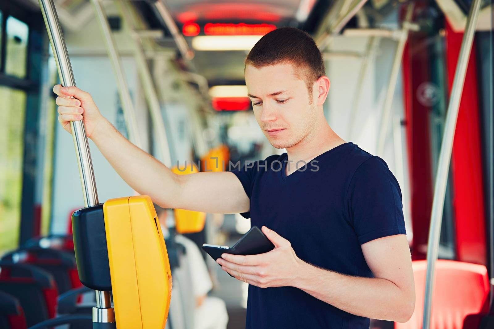 Everyday life and commuting to work by bus (tram). Handsome man is paying transport ticket with mobile phone. 