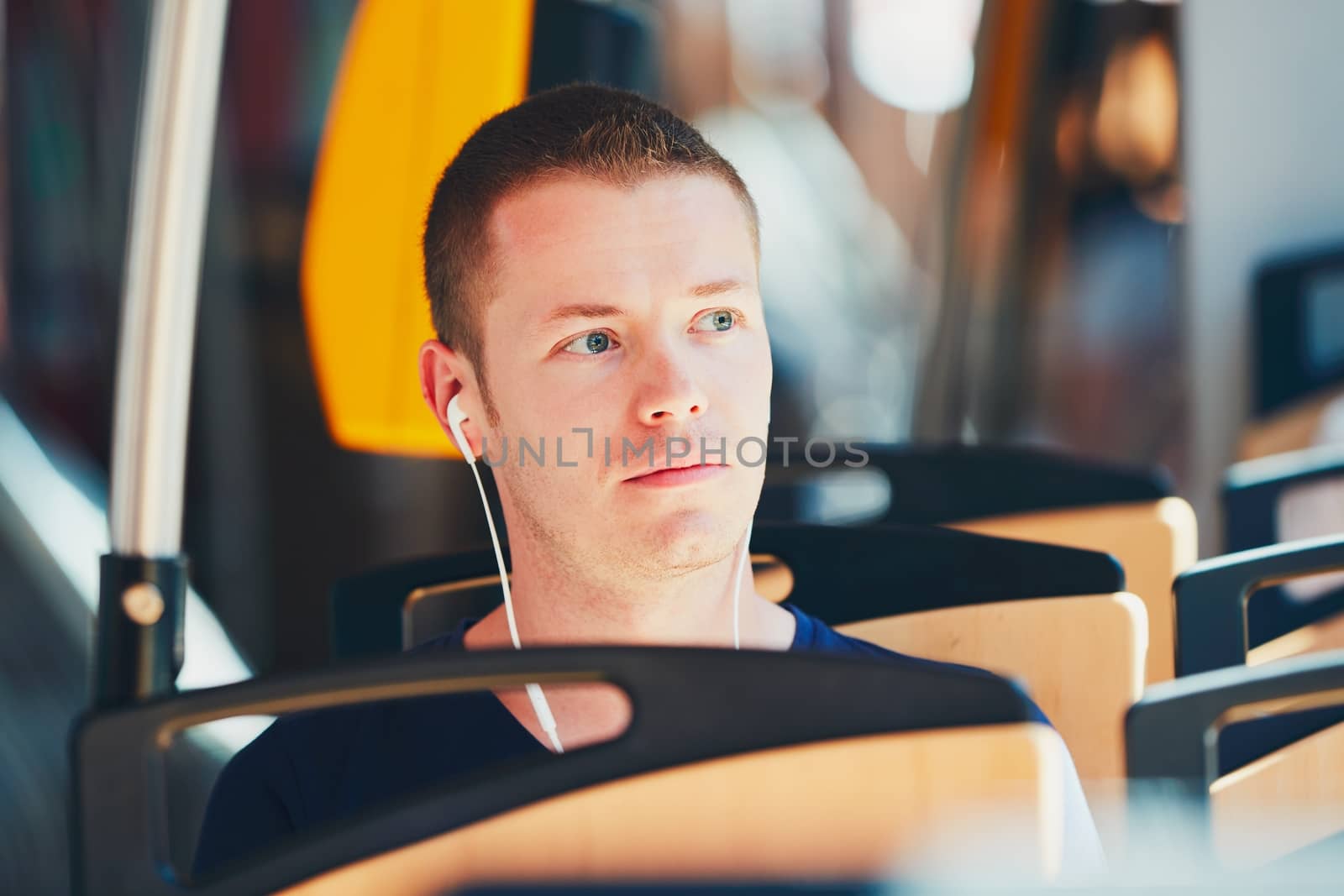 Everyday life and commuting to work by public transportation. Handsome young man is traveling by tram. Man is wearing headphones and listening to music.