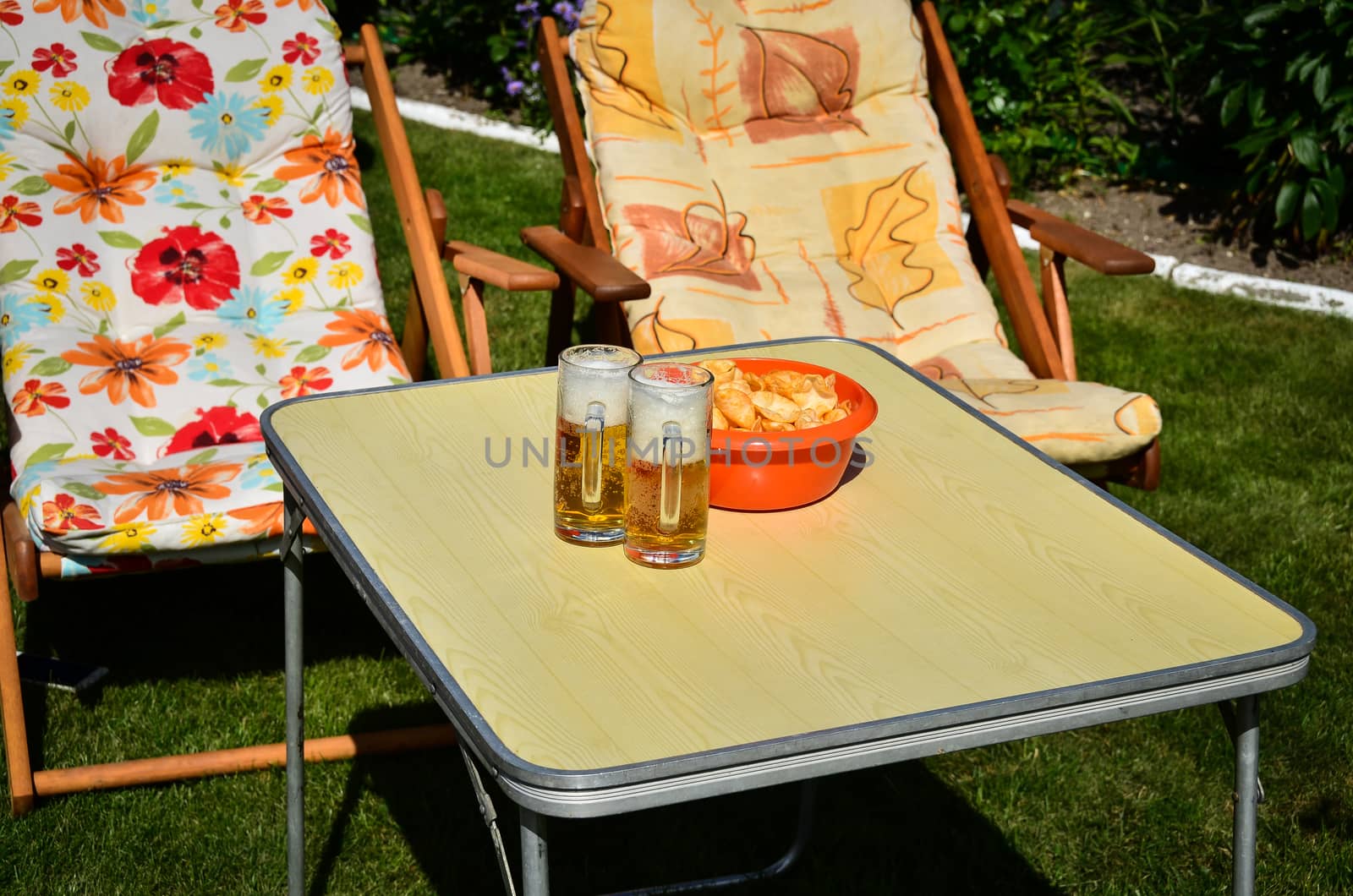 A glass of beer and a bowl of crisps on a table in the garden.