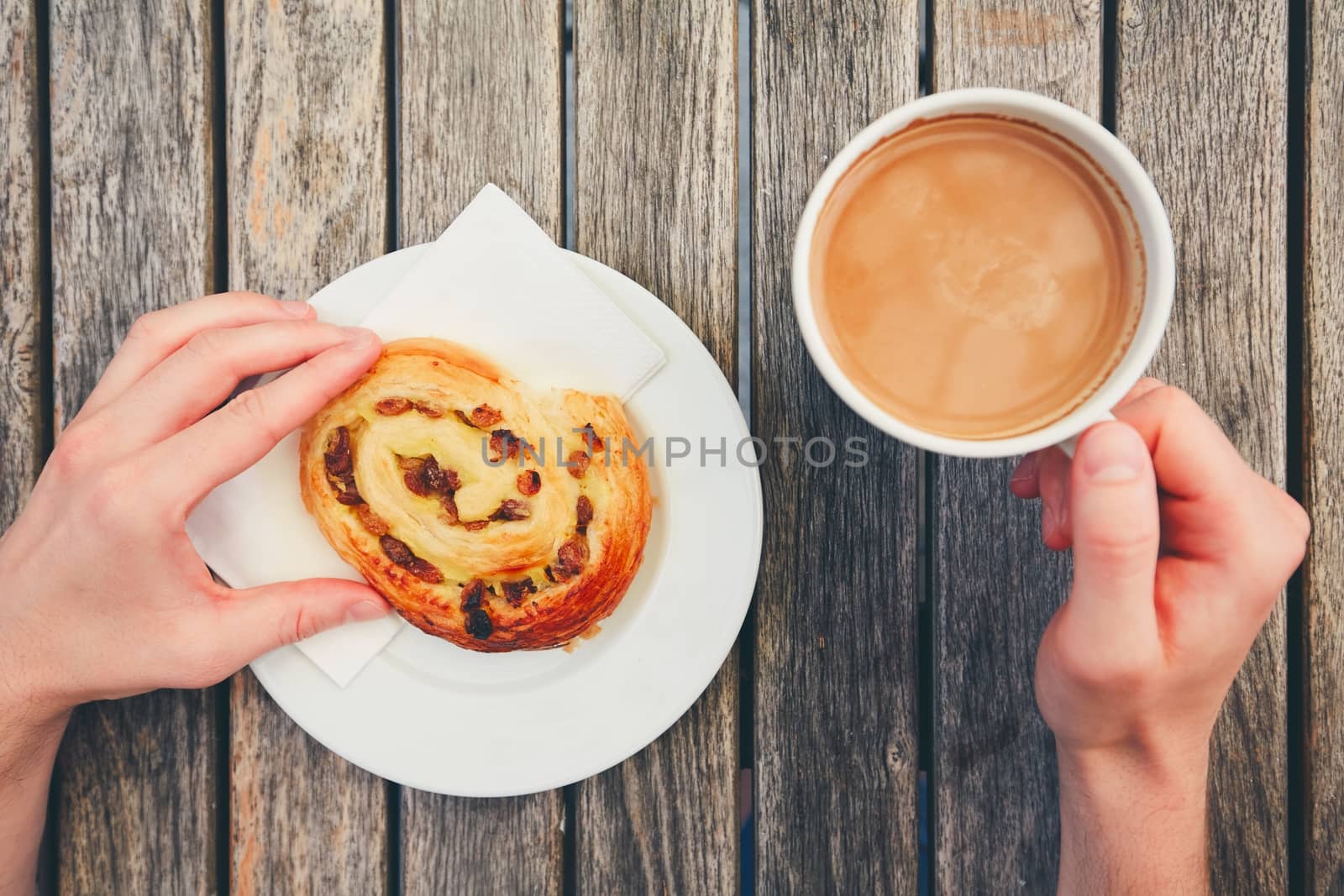 Morning coffee with with sweet pastries. Breakfast of the young man. Top view of snack and hands holding cup of hot drink on wooden desk. 