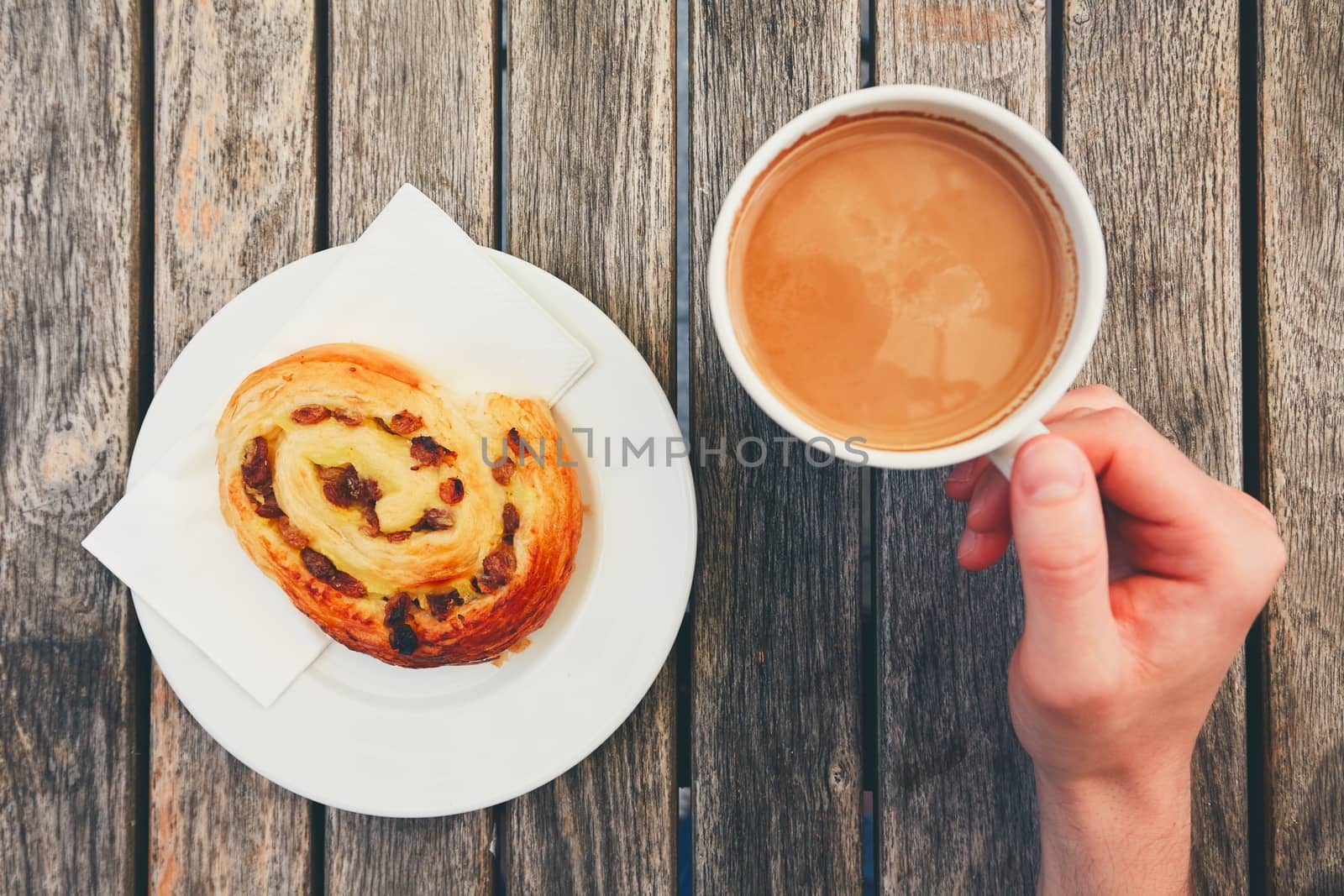 Morning coffee with with sweet pastries. Breakfast of the young man. Top view of snack and hands holding cup of hot drink on wooden desk. 