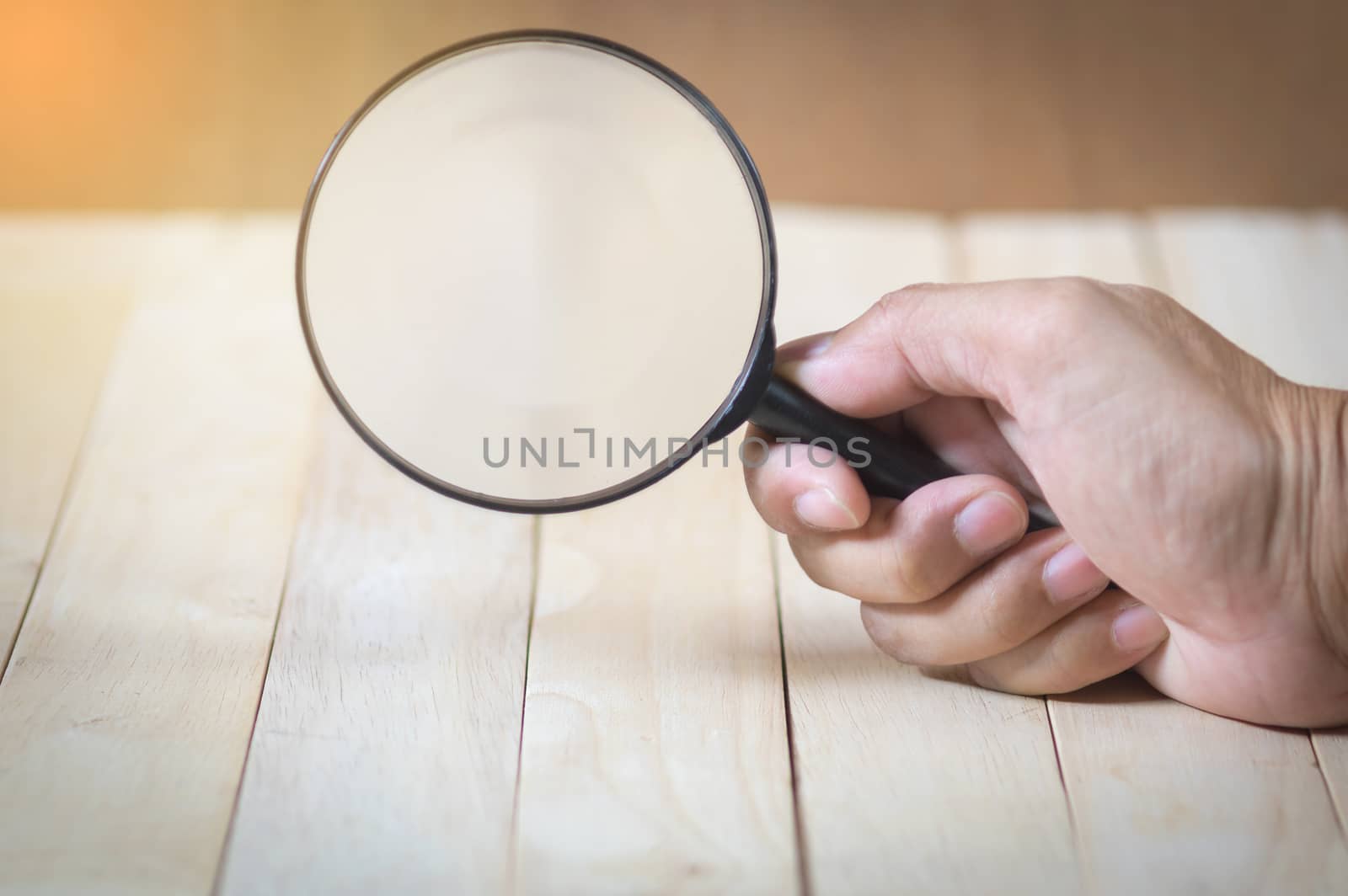 hand holding a magnifier glass. wood table background.