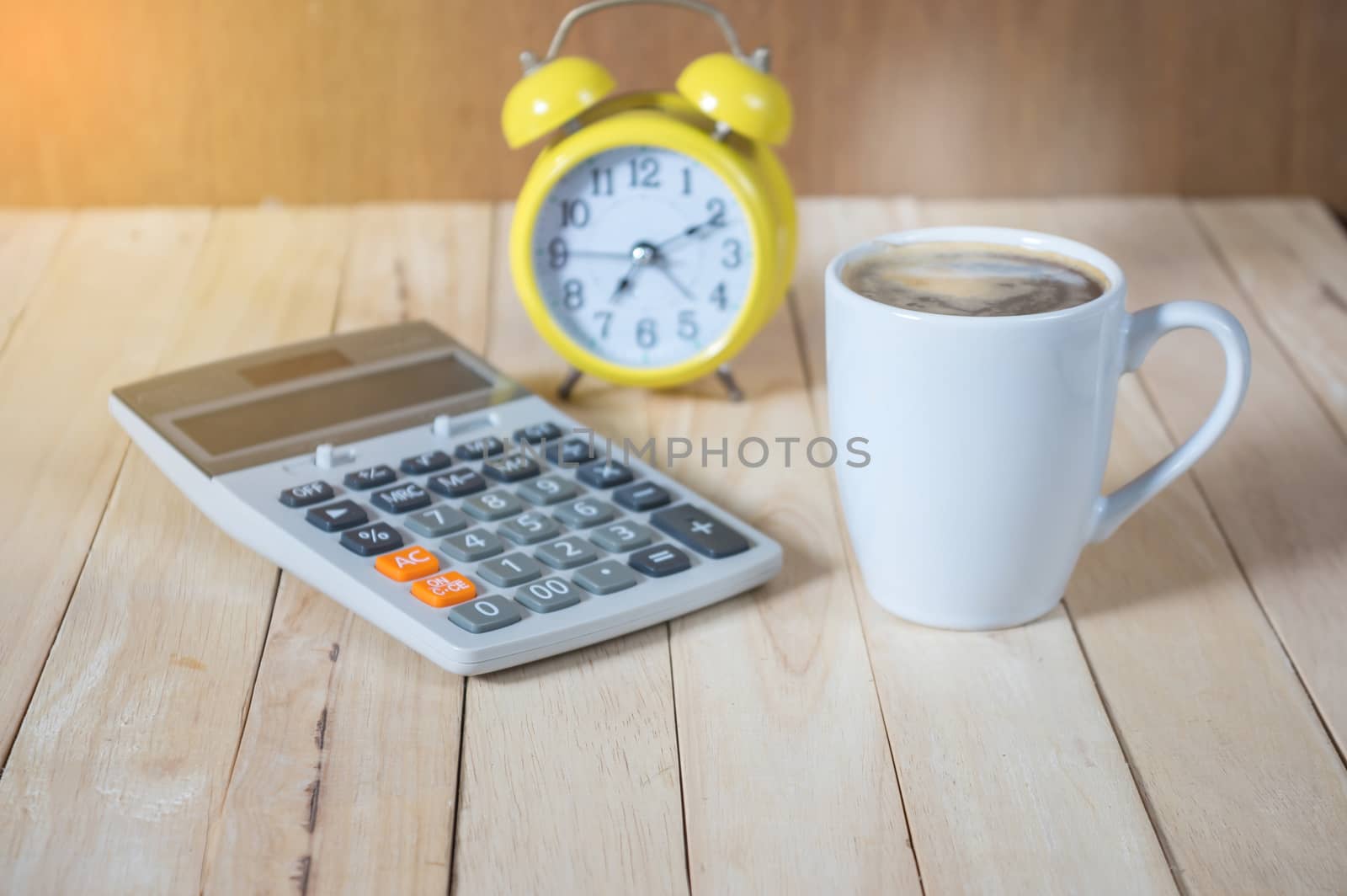 A cup of coffee on the table with calculator and clock.