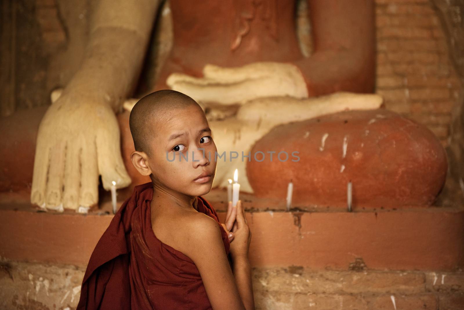 Portrait of young novice monk praying with candle light inside a Buddhist temple, Bagan, Myanmar.