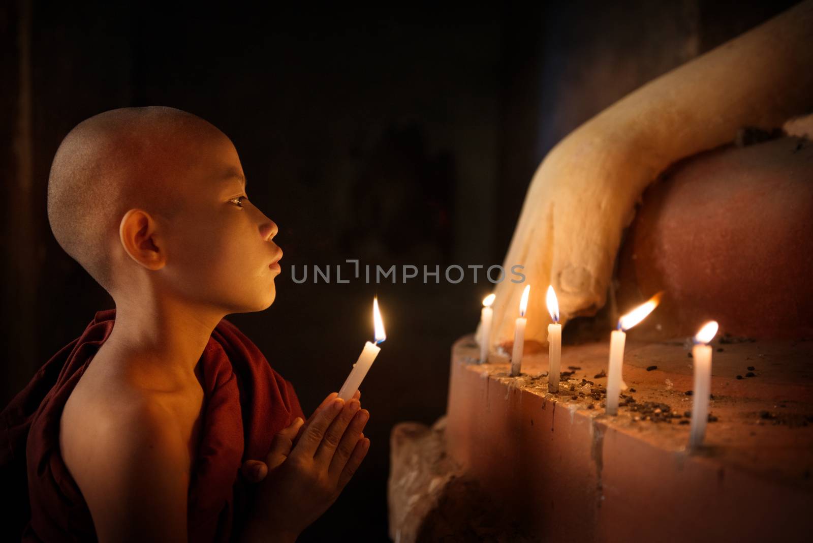 Portrait of young novice monk praying with candlelight inside a Buddhist temple, low light setting, Bagan, Myanmar.