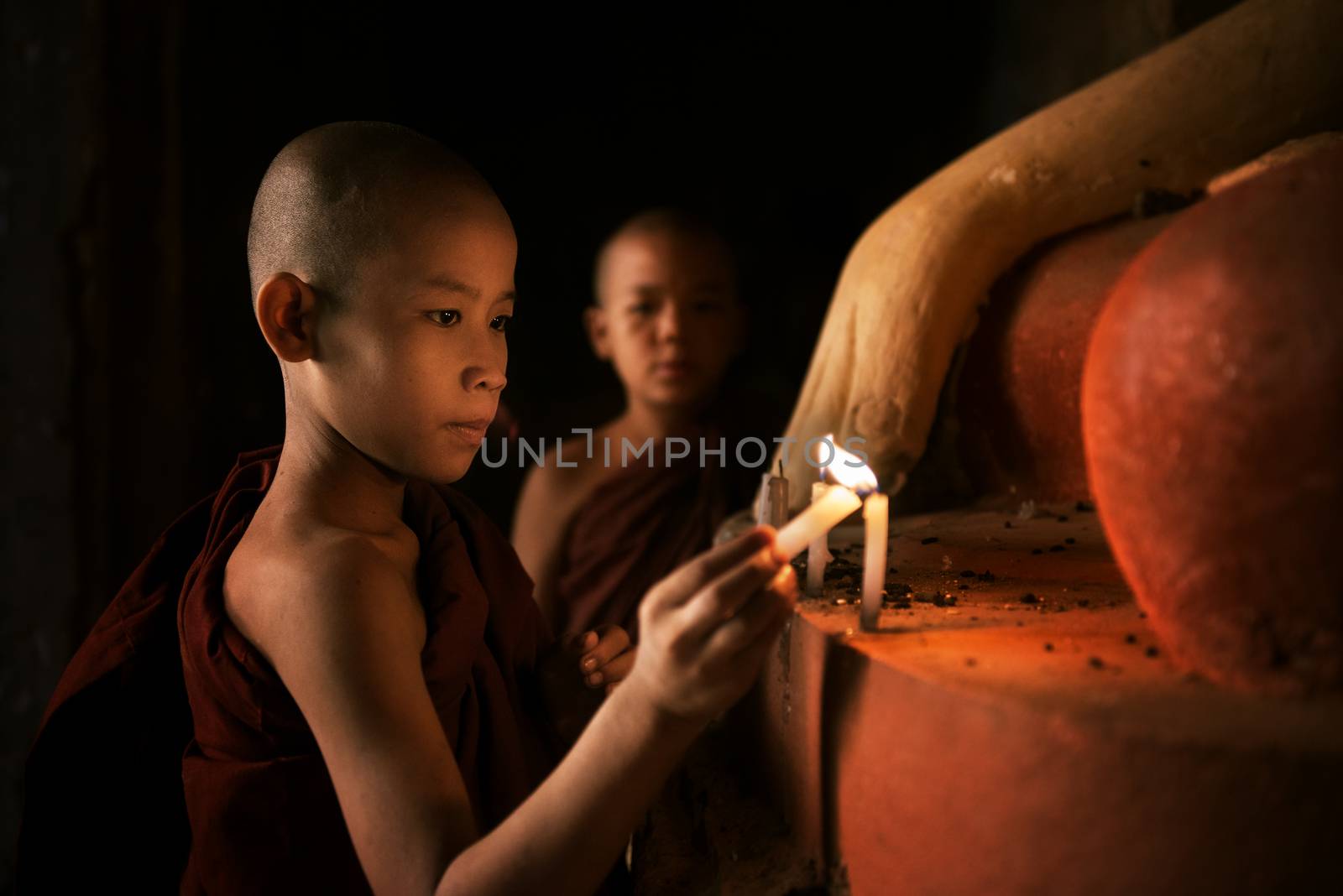 Portrait of young novice monks lighting up candlelight inside a Buddhist temple, low light setting, Bagan, Myanmar.