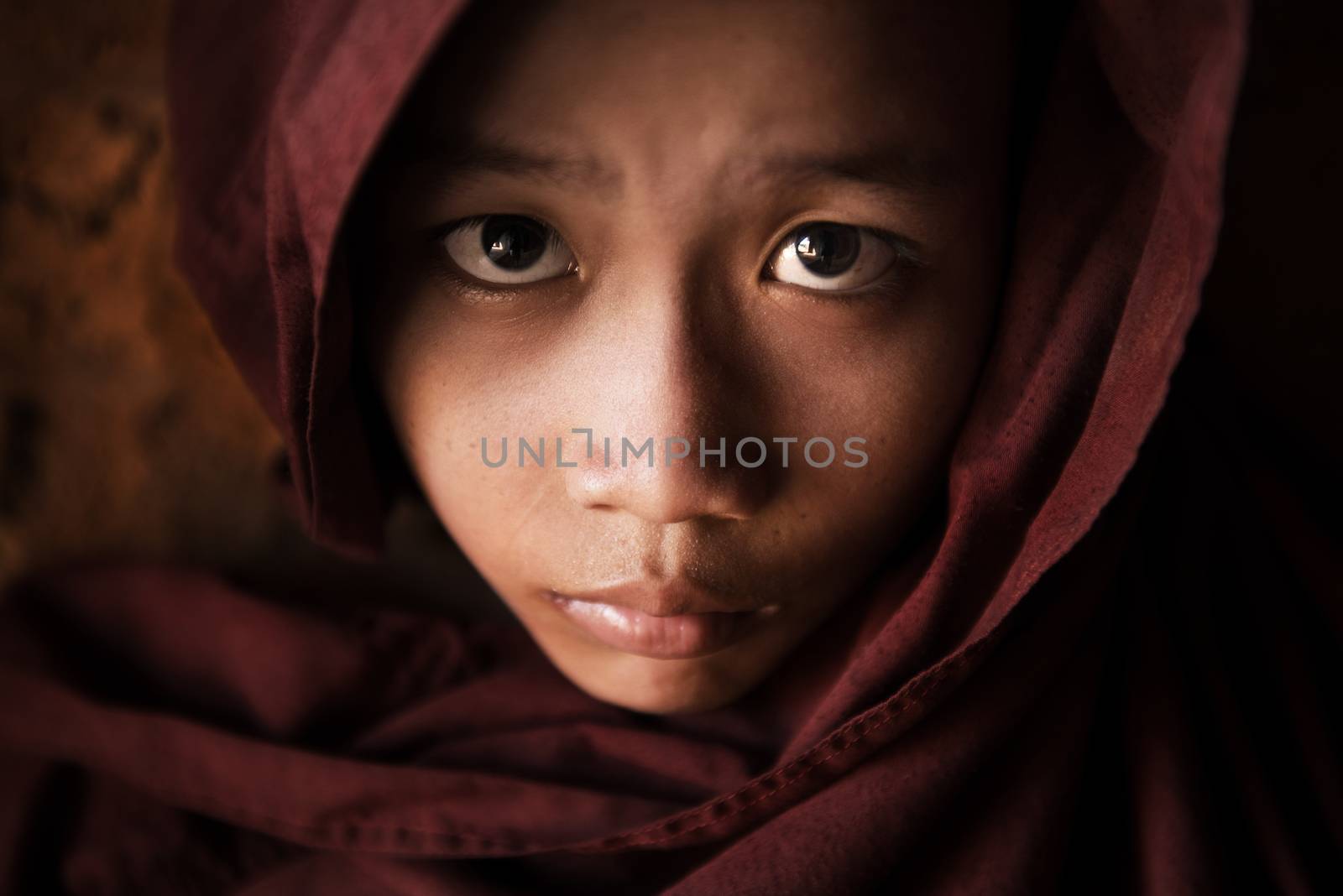 Close up face of  young novice monk covered with robe, low light with noise setting, Bagan, Myanmar.