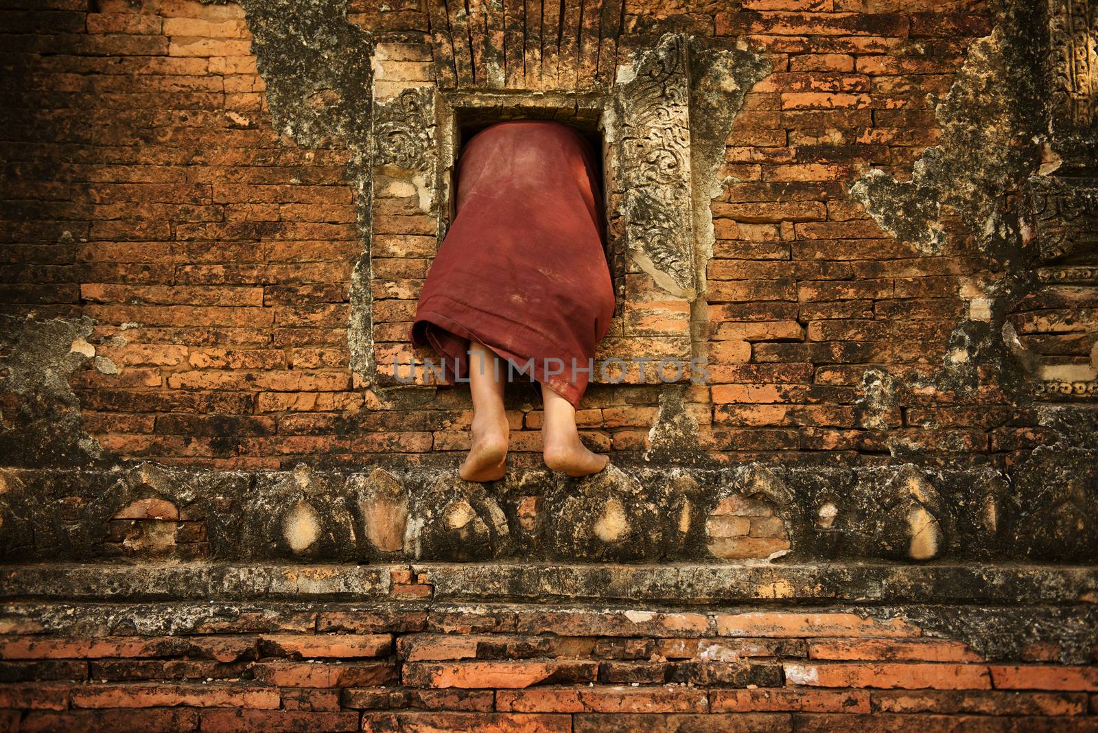 Young novice monks climbing into Buddhist temple from window, Bagan, Myanmar.