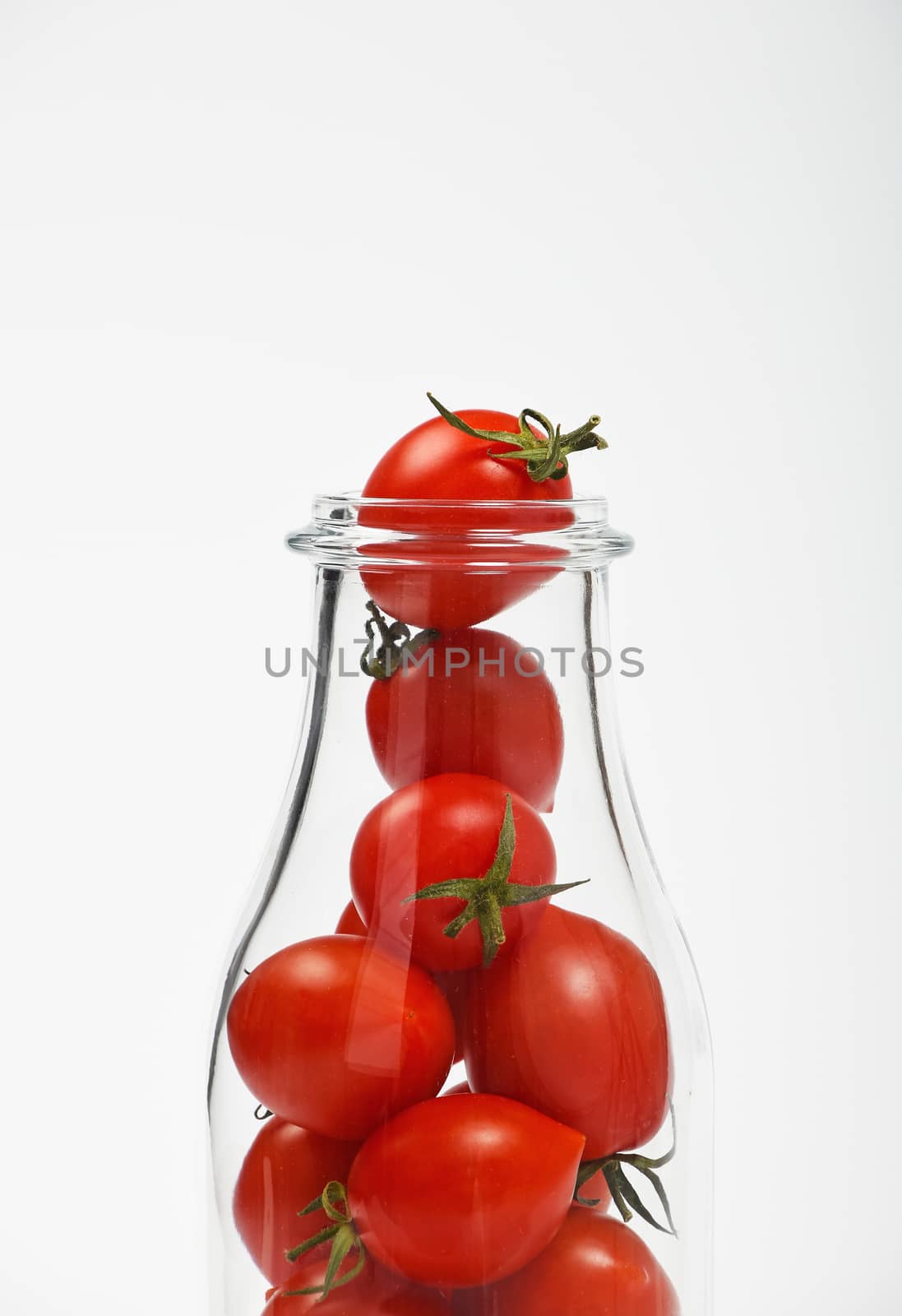 Big glass bottle full of cherry tomatoes over white background as symbol of fresh natural organic juice or ketchup, close up crop