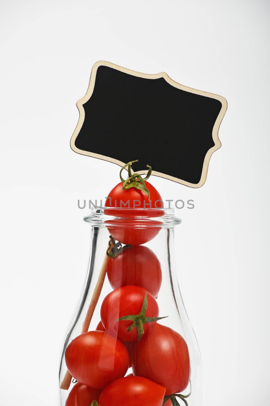 Big glass bottle full of cherry tomatoes and black chalkboard sign over white background as symbol of fresh natural organic juice or ketchup, close up crop