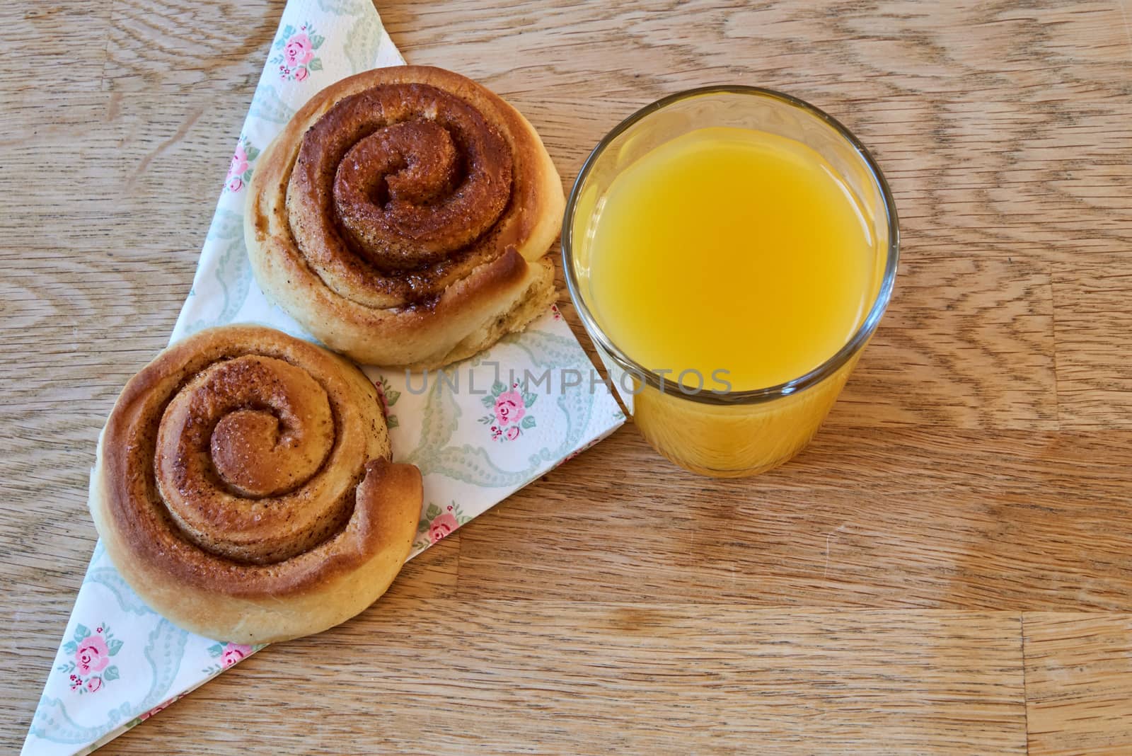 Fresh cinnamon buns on a napkin with a glass of orange juice.