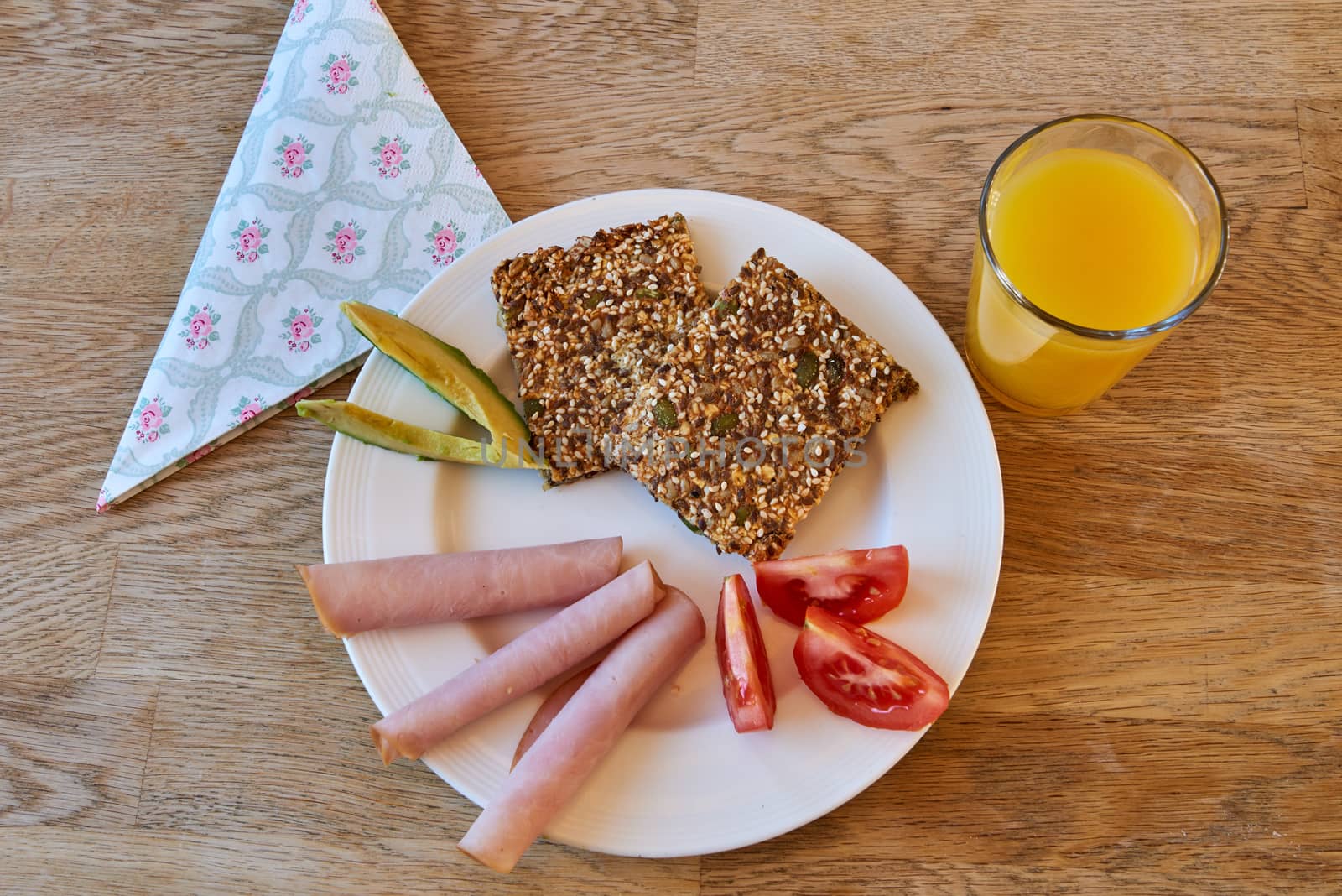 Breakfast plate with healthy food, crispbread, avocado, tomato, ham and a glass of orange juice.