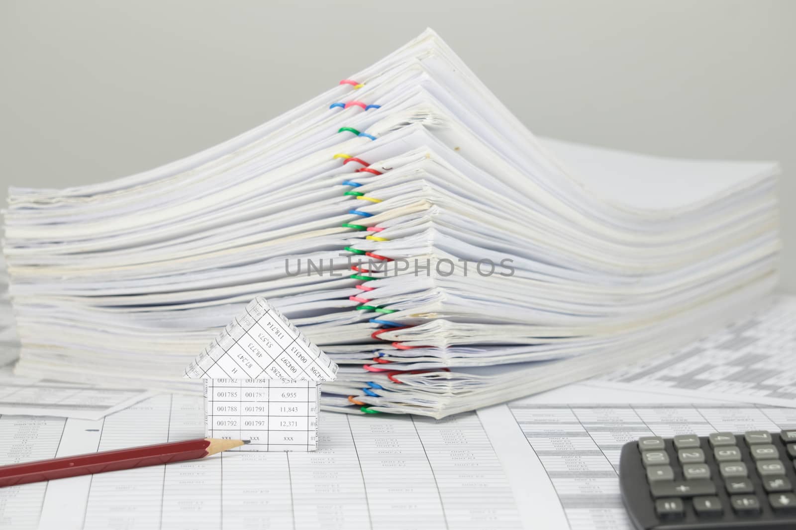 House and pencil on finance account have blur pile overload paperwork of report and receipt with colorful paperclip and calculator place on white background.