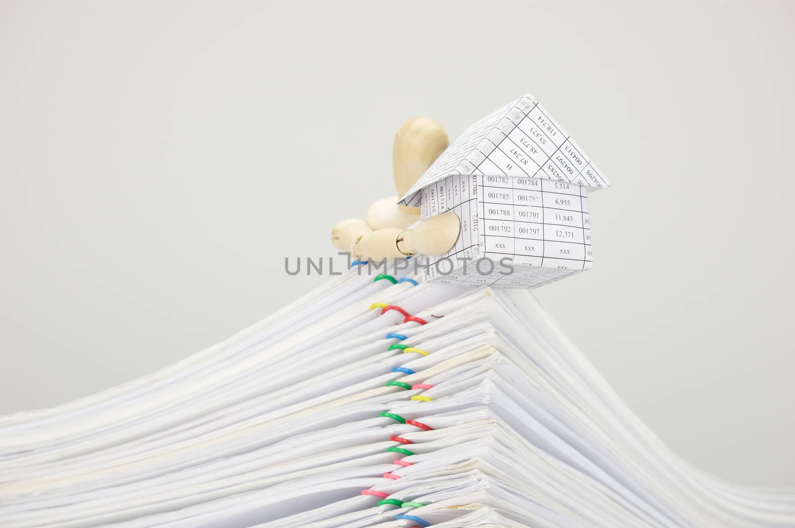 Wooden dummy holding house on top of pile overload document of report and receipt with colorful paperclip with white background.