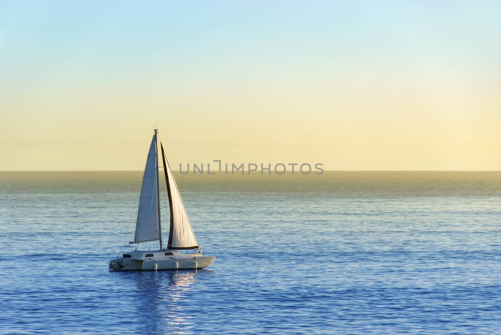 Sailboat on in the sunset gliding over the calm ocean surface.