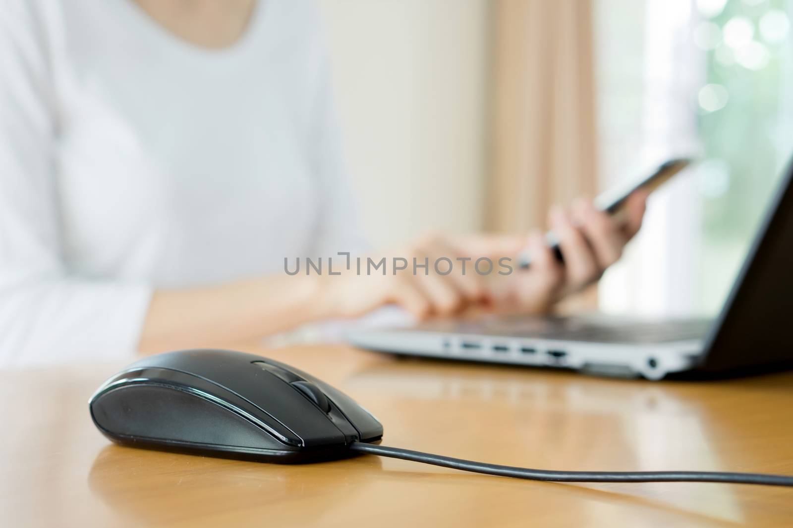 busy young woman is typing on laptop computer and using mobile phone at the same time