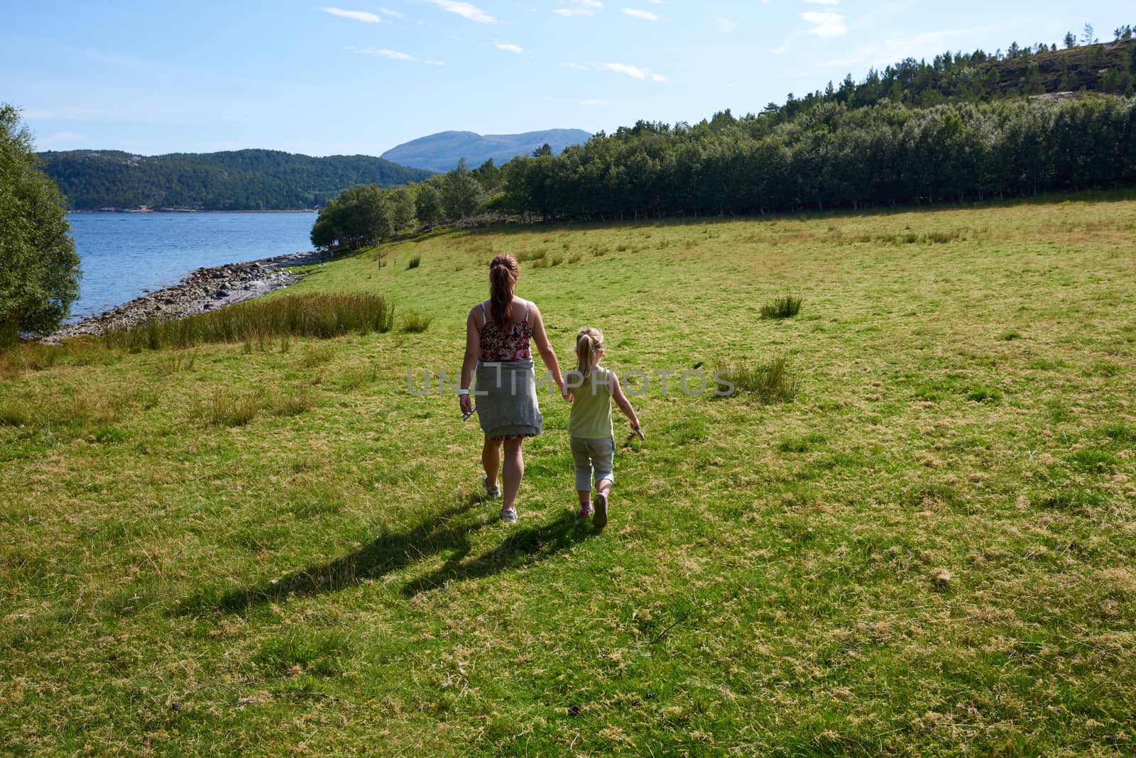 Mother and daughter holding hands in a grassy green field.