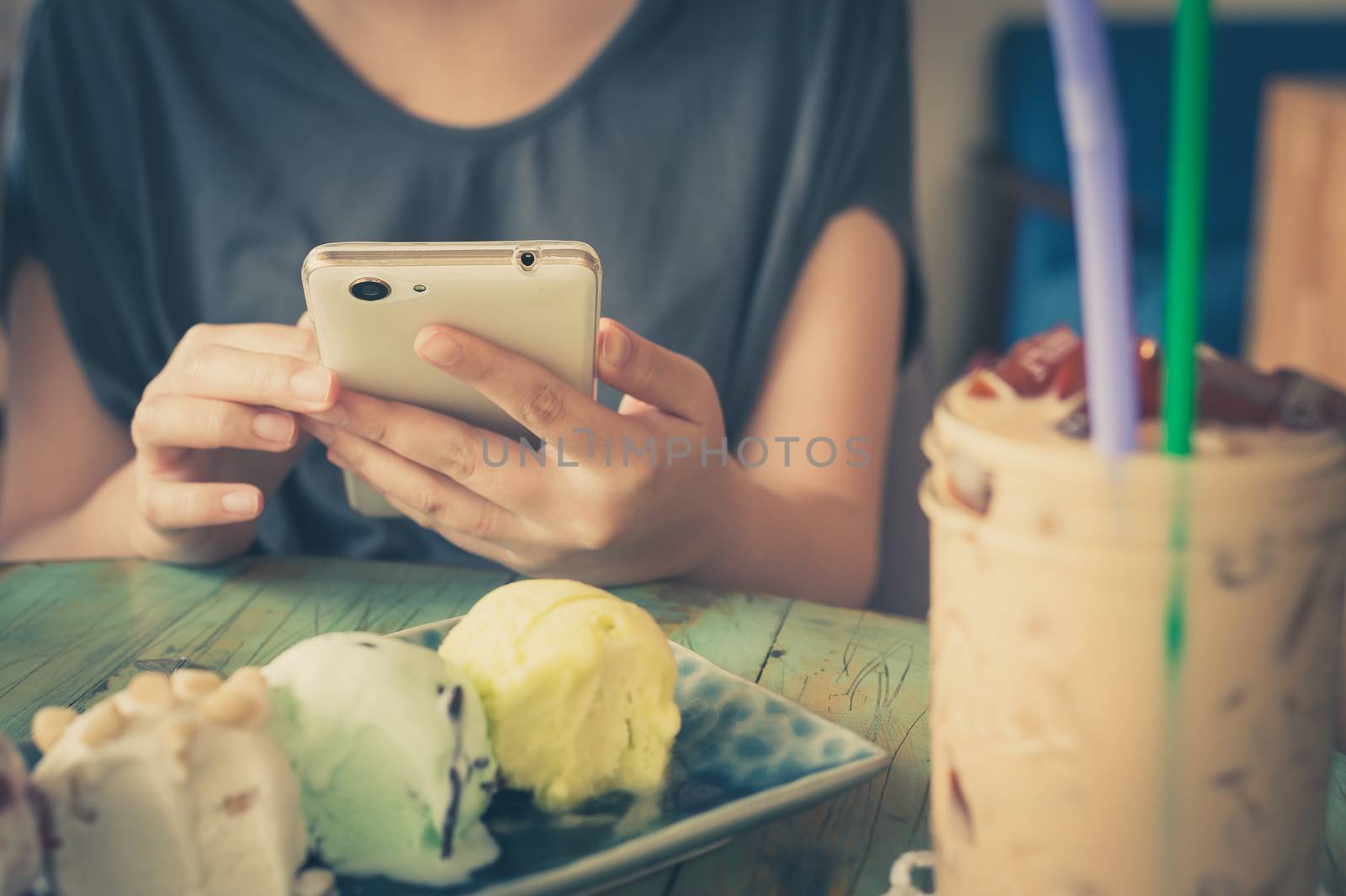 Afternoon scene of young woman using smartphone for social networking in ice cream cafe on weekend. Modern lifestyle with technology concept. processed with vintage filter effect