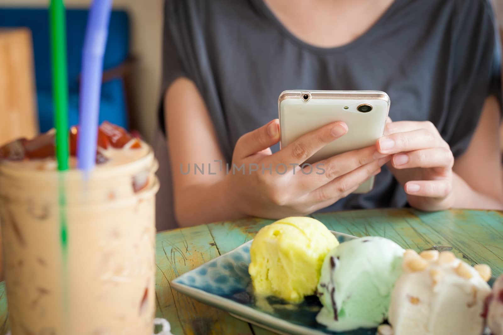Afternoon scene of young woman using smartphone for social networking in ice cream cafe on weekend. Modern lifestyle with technology concept.