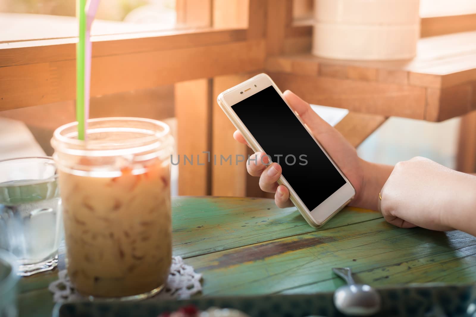 Woman hand holding smartphone on wood table in cafe on weekend afternoon. Trendy lifestyle concept with communication technology.