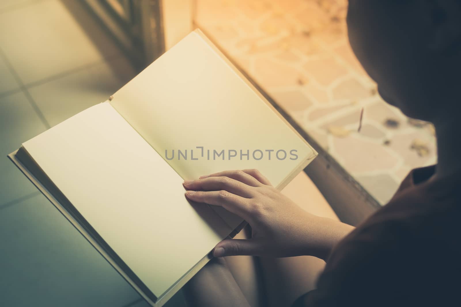 Young woman reading blank book while sitting beside window in morning time on weekend. Morning lifestyle on weekend concept with vintage filter effect