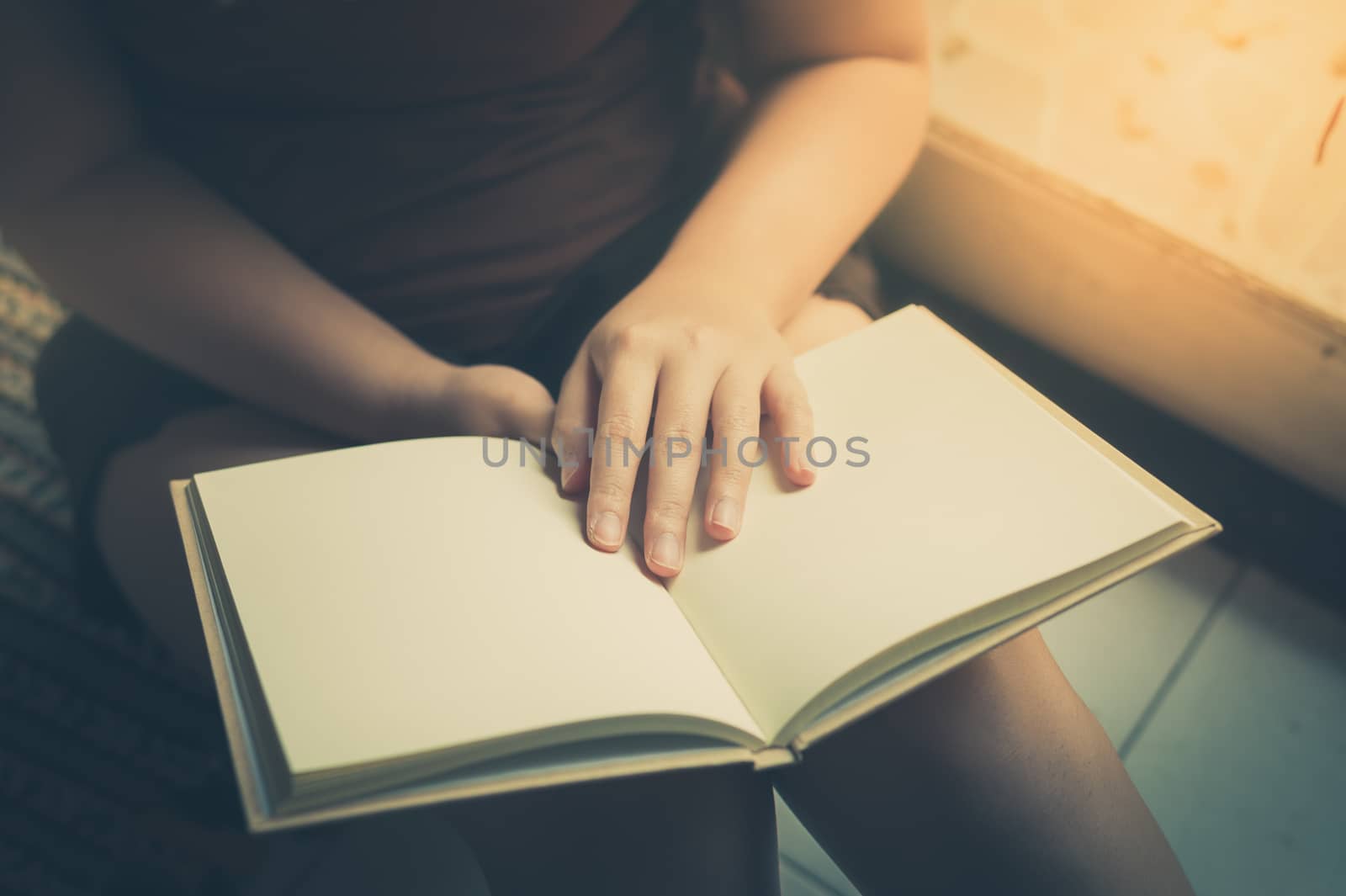 Young woman reading blank book while sitting beside window in morning time on weekend. Morning lifestyle on weekend concept with vintage filter effect