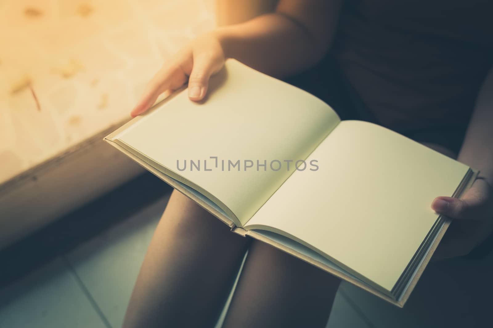 Young woman reading blank book while sitting beside window in morning time on weekend. Morning lifestyle on weekend concept with vintage filter effect