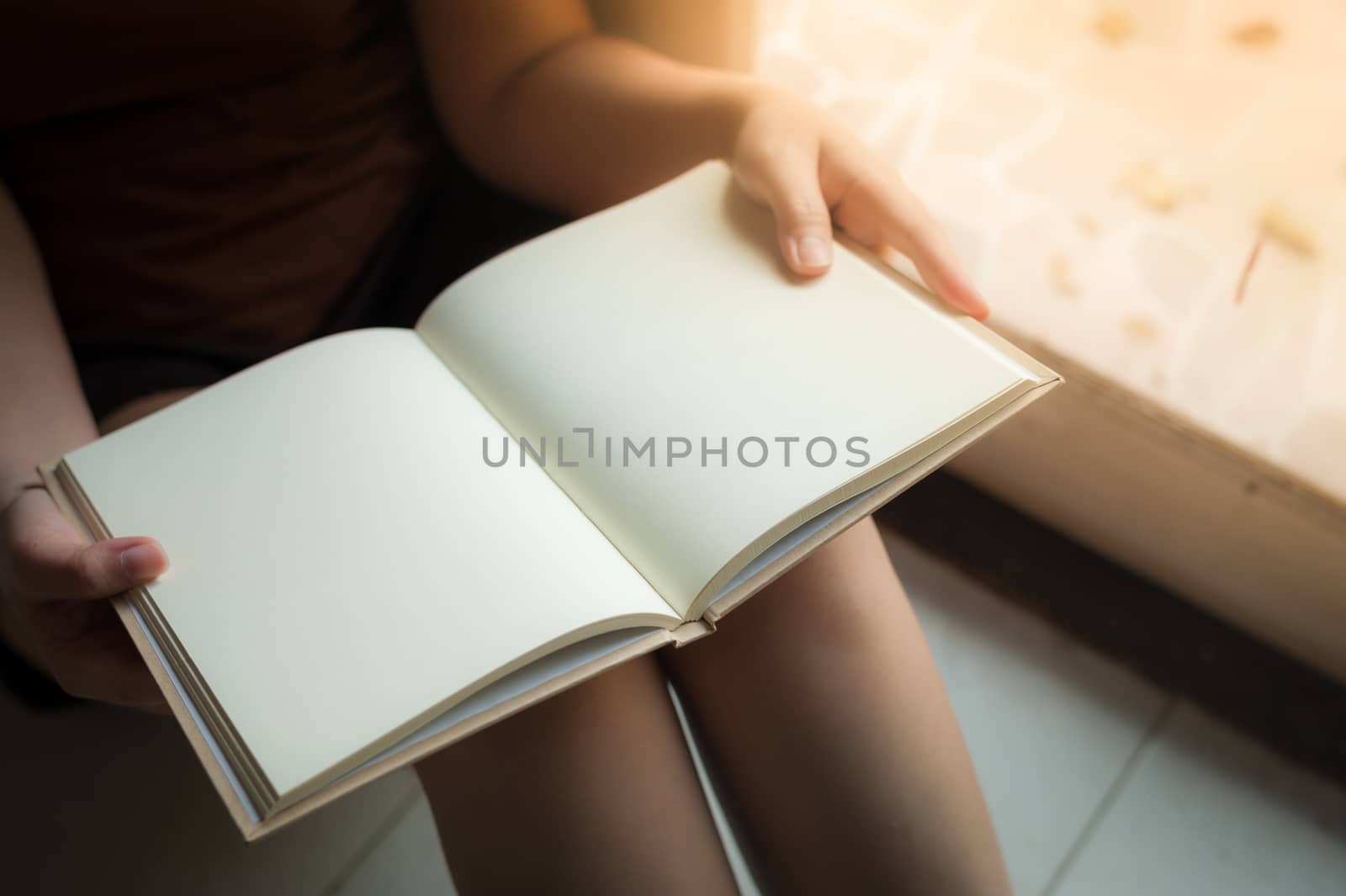 Young woman reading blank book while sitting beside window in morning time on weekend. Morning lifestyle on weekend concept.