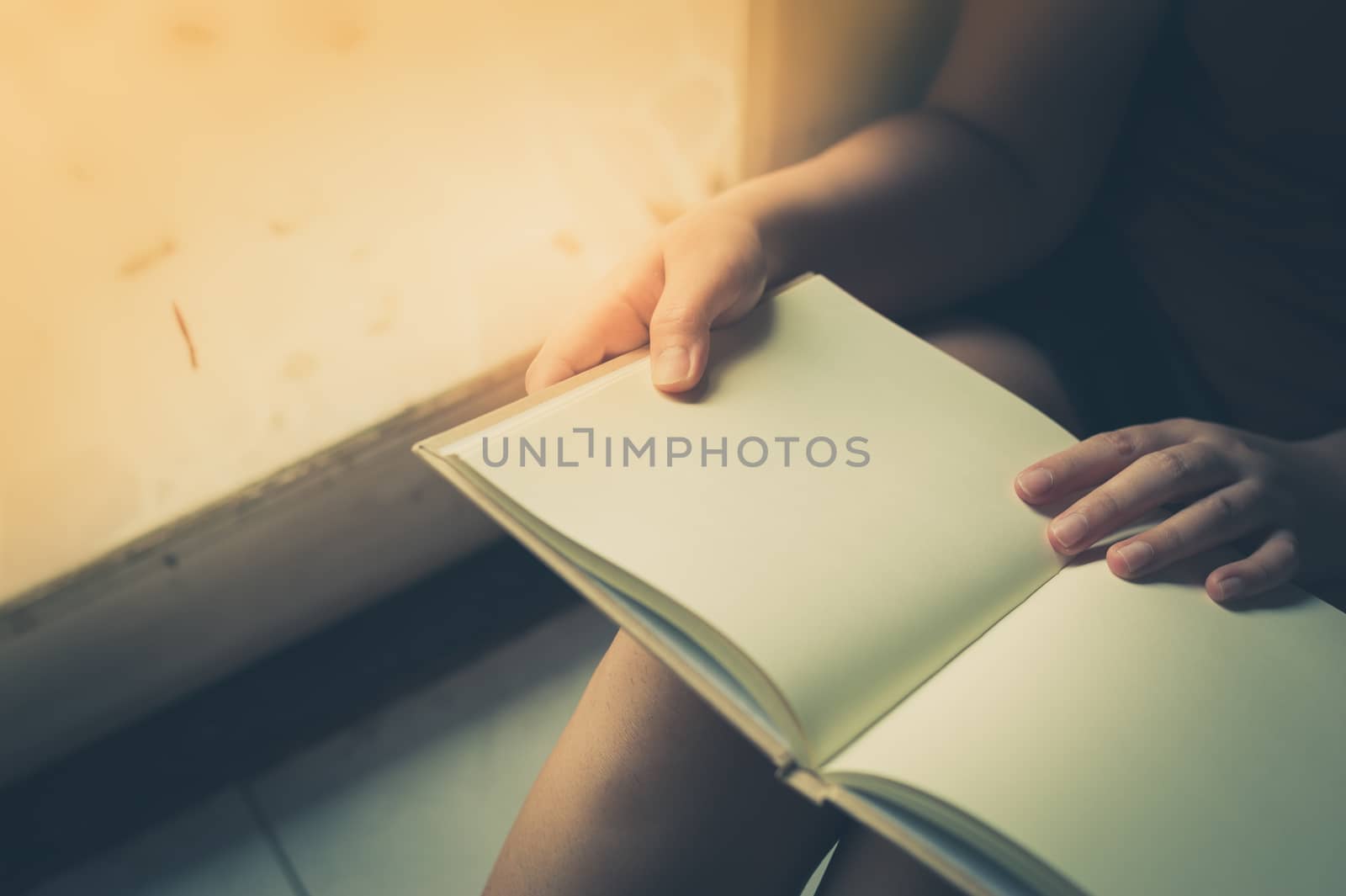 Young woman reading blank book while sitting beside window in morning time on weekend. Morning lifestyle on weekend concept with vintage filter effect