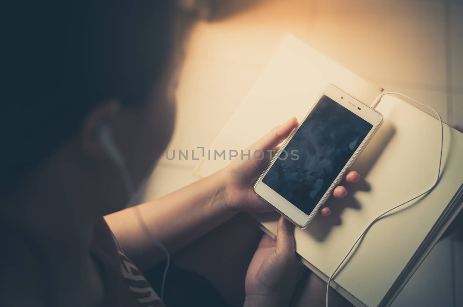 Young woman listening music with smartphone while reading book in morning time on weekend. Morning lifestyle with technology on weekend concept with vintage filter effect