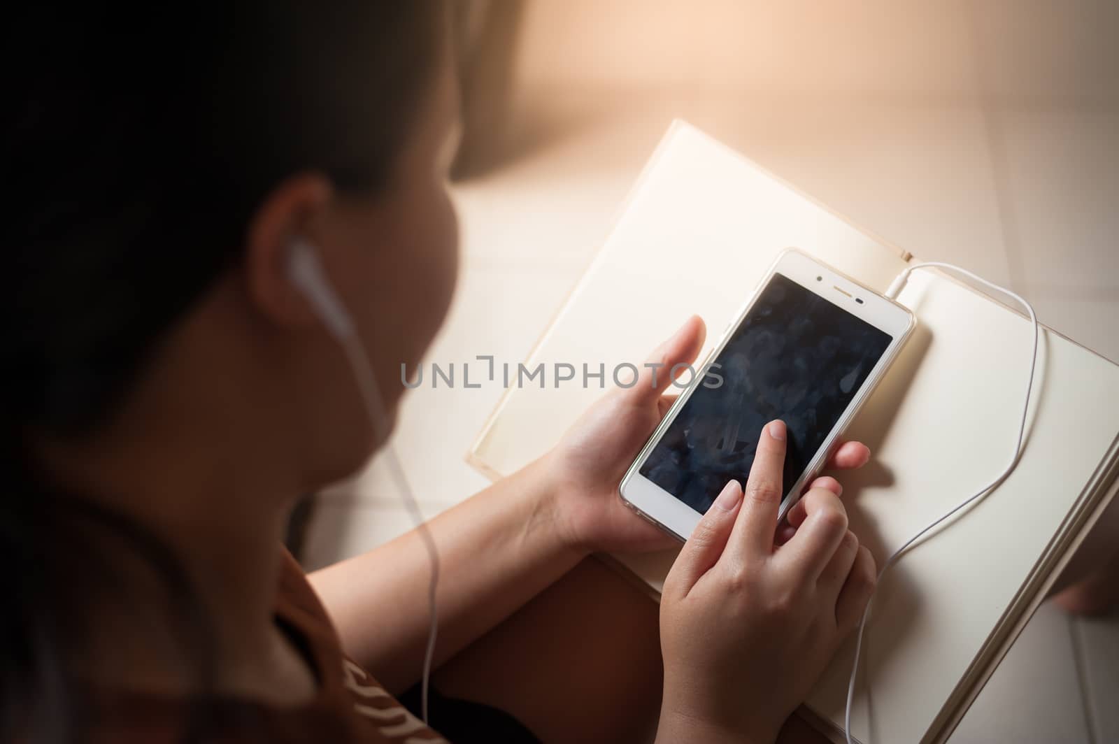 Young woman listening music with smartphone and touching on screen while reading book in morning time on weekend. Morning lifestyle with technology on weekend concept.