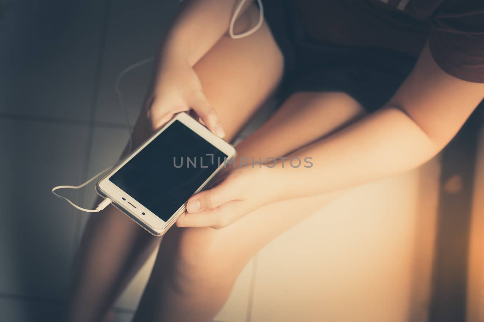Young woman listening music with smartphone while sitting beside window in morning time on weekend. Morning lifestyle with technology on weekend concept with vintage filter effect