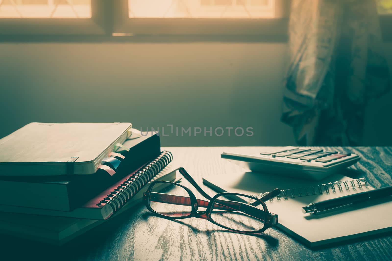 Glasses put down on table beside notebooks and pen in morning time on work day. Freelance business working concept with vintage filter effect