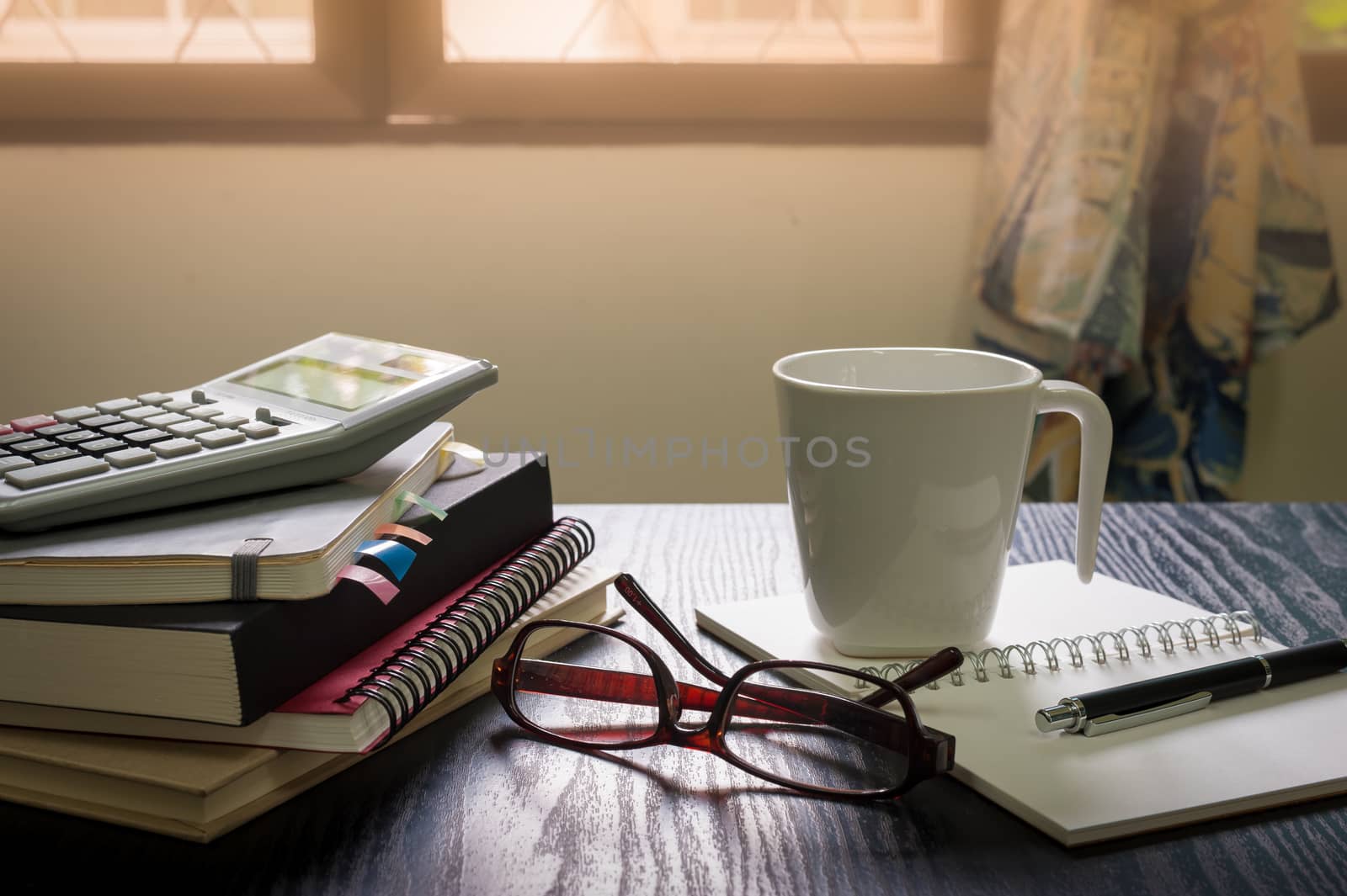 Coffee cup put down on table beside notebooks, glasses, and pen in morning time on work day. Freelance business working concept