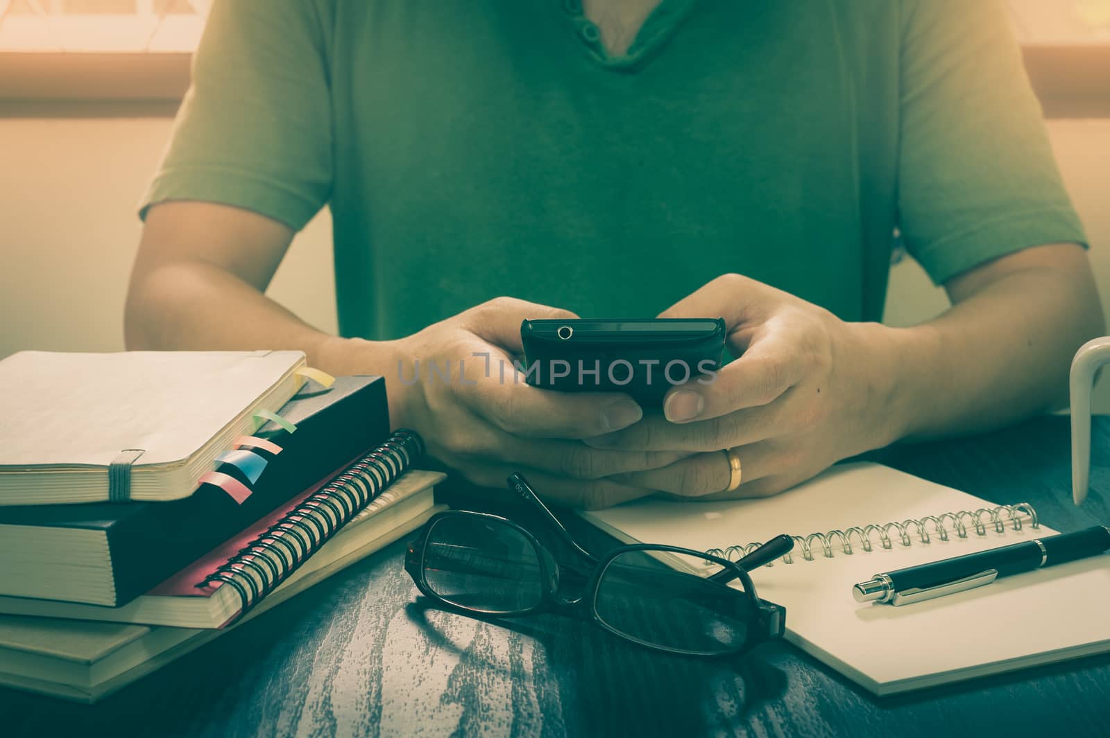 Young freelance man using smartphone for business on working desk in morning time on work day. Working at home concept with vintage filter effect