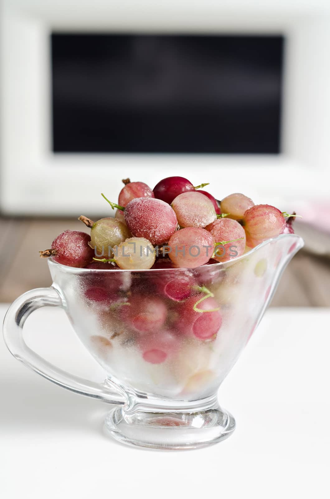 Frozen gooseberries in a glass Cup on the background of microwave oven.