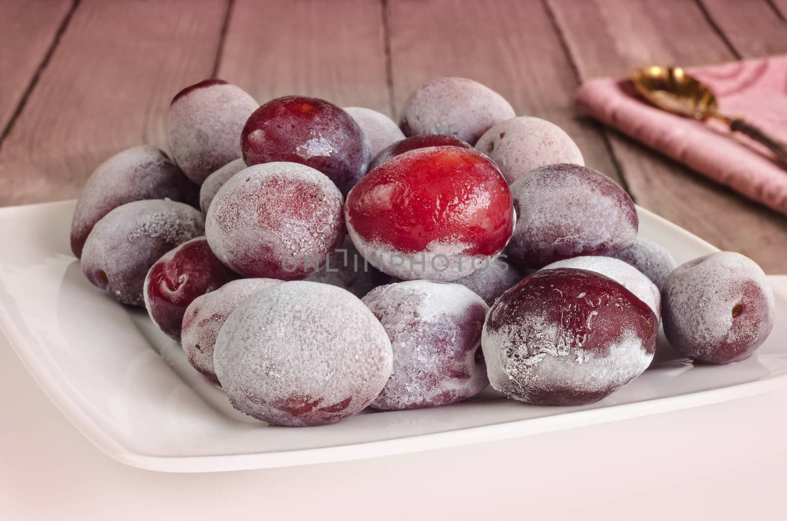 Frozen plums on plate, on wooden background toned in pink