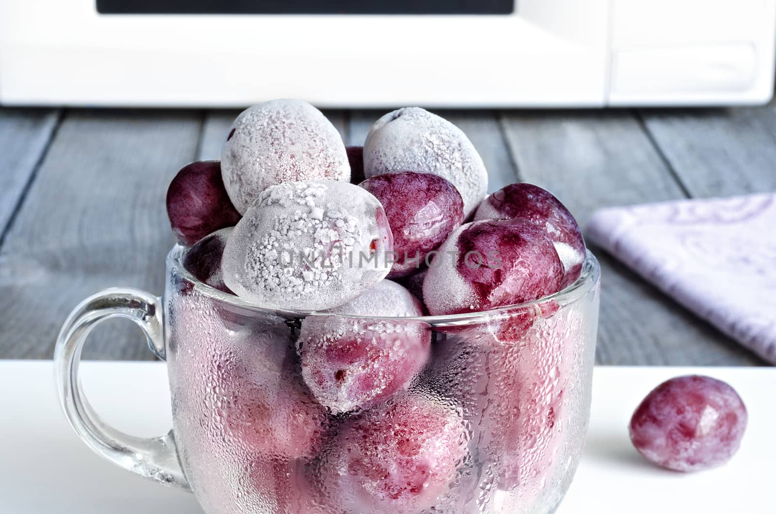 Frozen plums in a glass Cup on the background of the microwave.