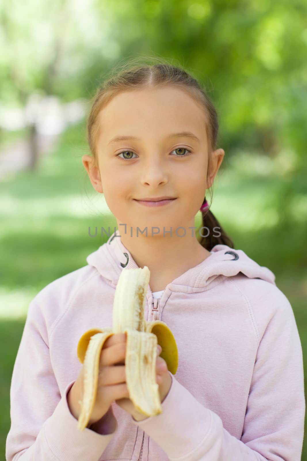 Sunny girl with bananas. The child looks at the camera. Happily eating fruit