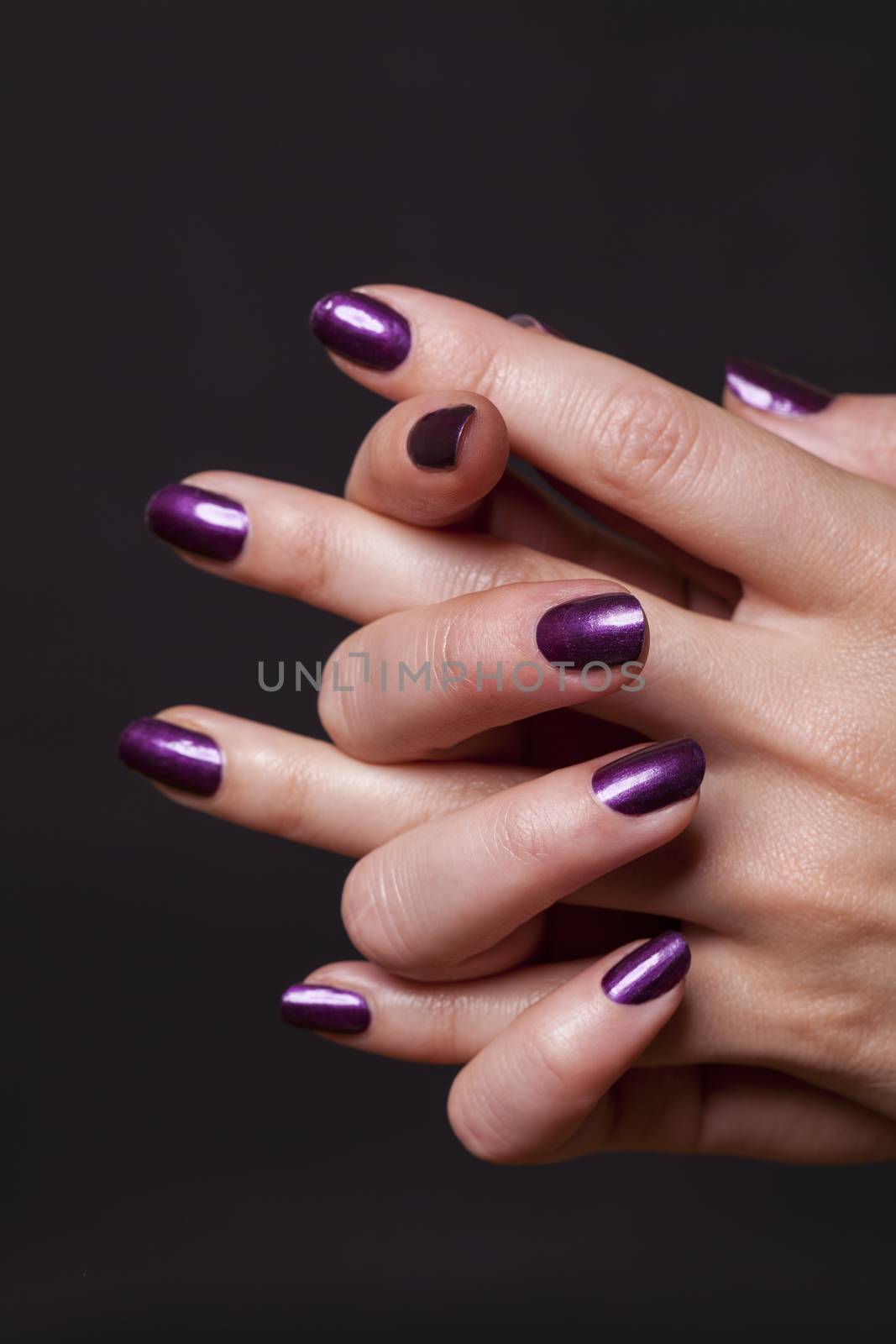 Close up of crossed over female hands decorated with purple fingernail paint over black