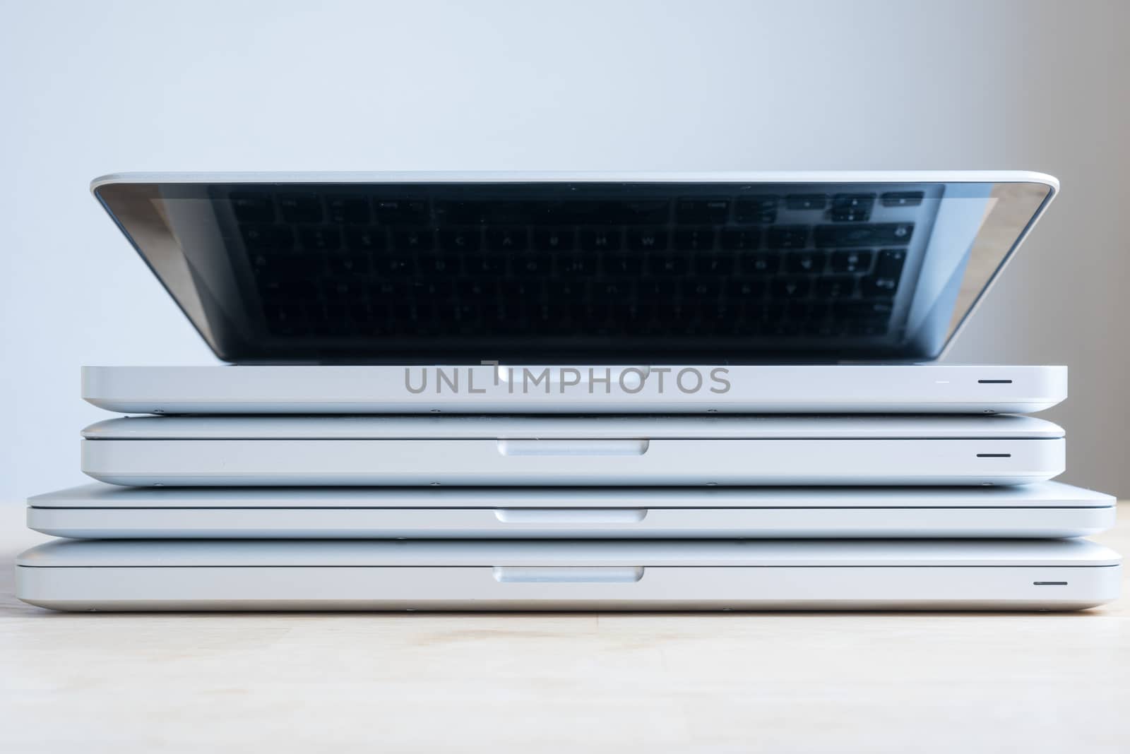 A bunch of aluminium laptops stacked on top of each other. The one on top is open.