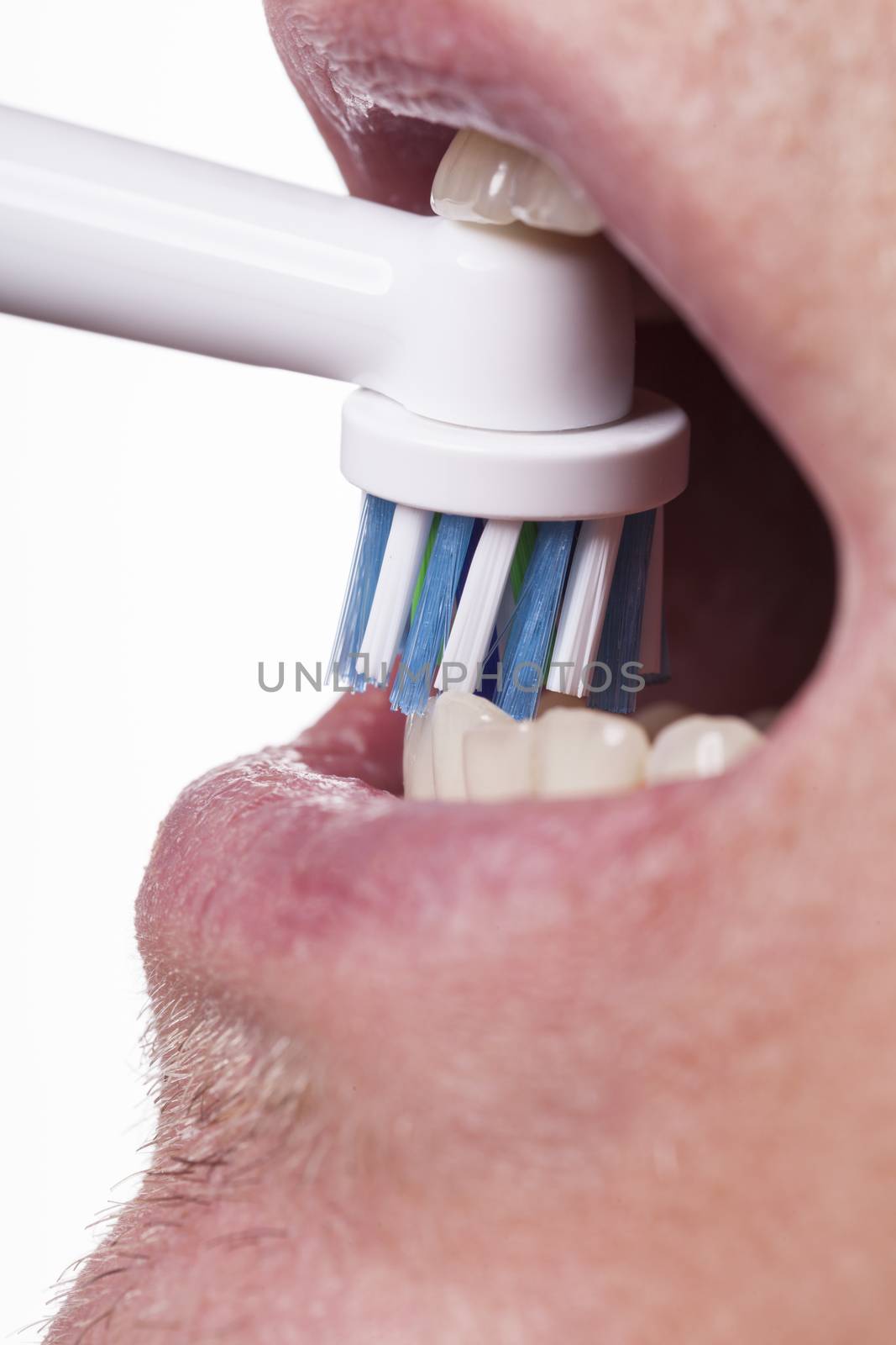 Close up of electric toothbrush with blue bristles and tube with paste bubbled at its opening on white background