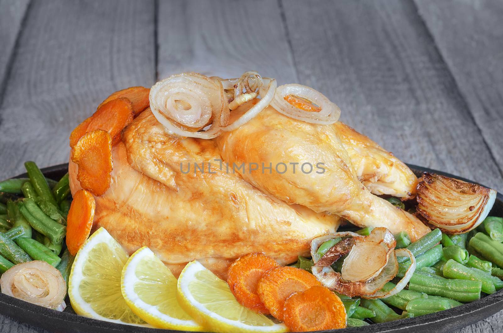 Fried chicken with vegetables in the pan, standing on the old boards