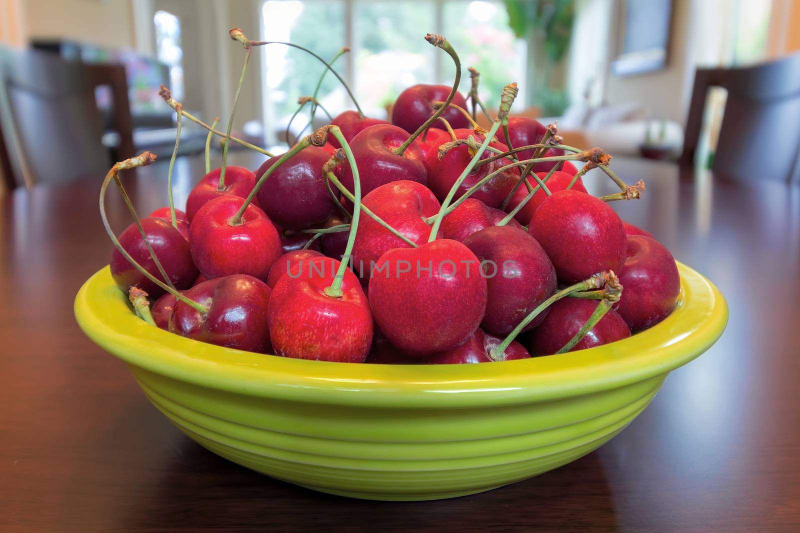 Pile of Bing Cherries in green bowl and on wood dining table