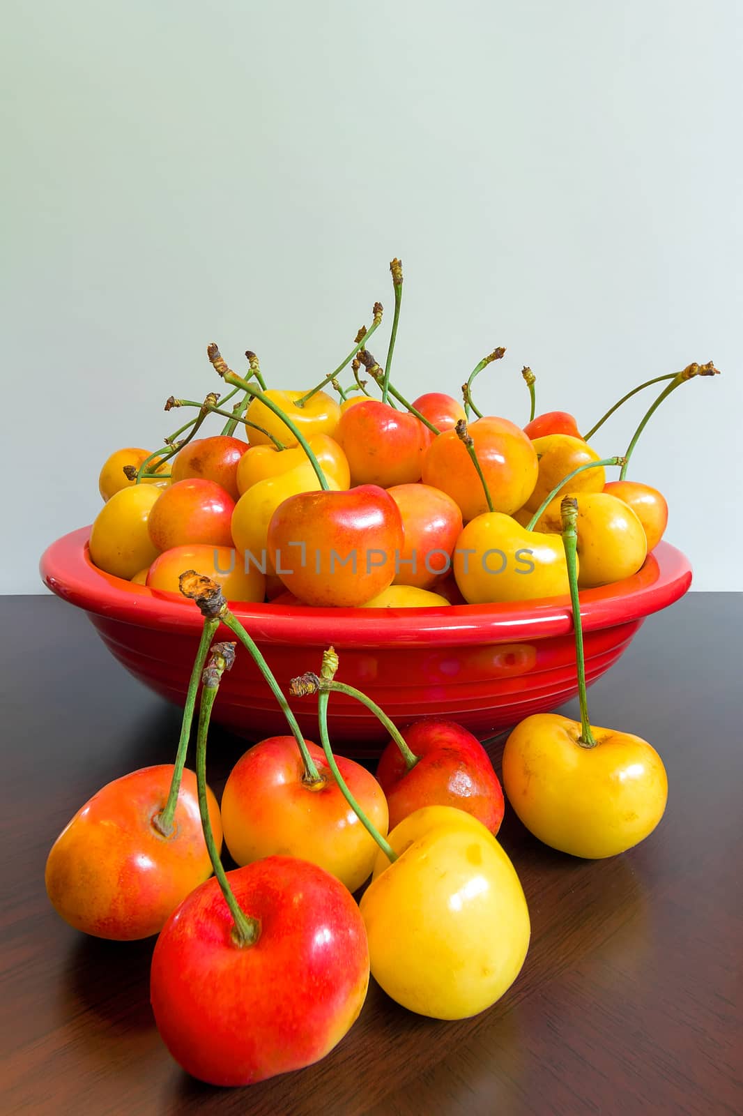 Pile of Rainier Cherries in a red bowl sitting on a wooden table